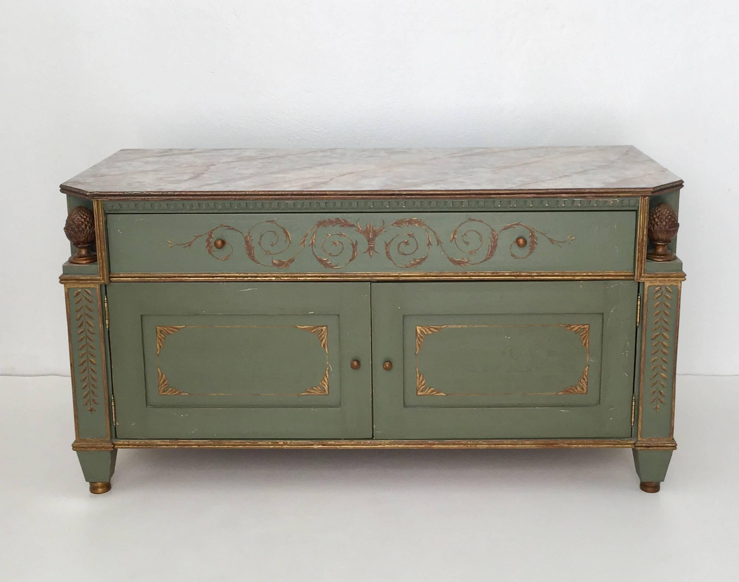Glamorous pair of neoclassical style painted commodes, circa 1950s-1960s. These stunning richly painted Gustavian green painted chests with faux painted marble tops are embellished with gilt decorative accents and are designed with a single pull-out