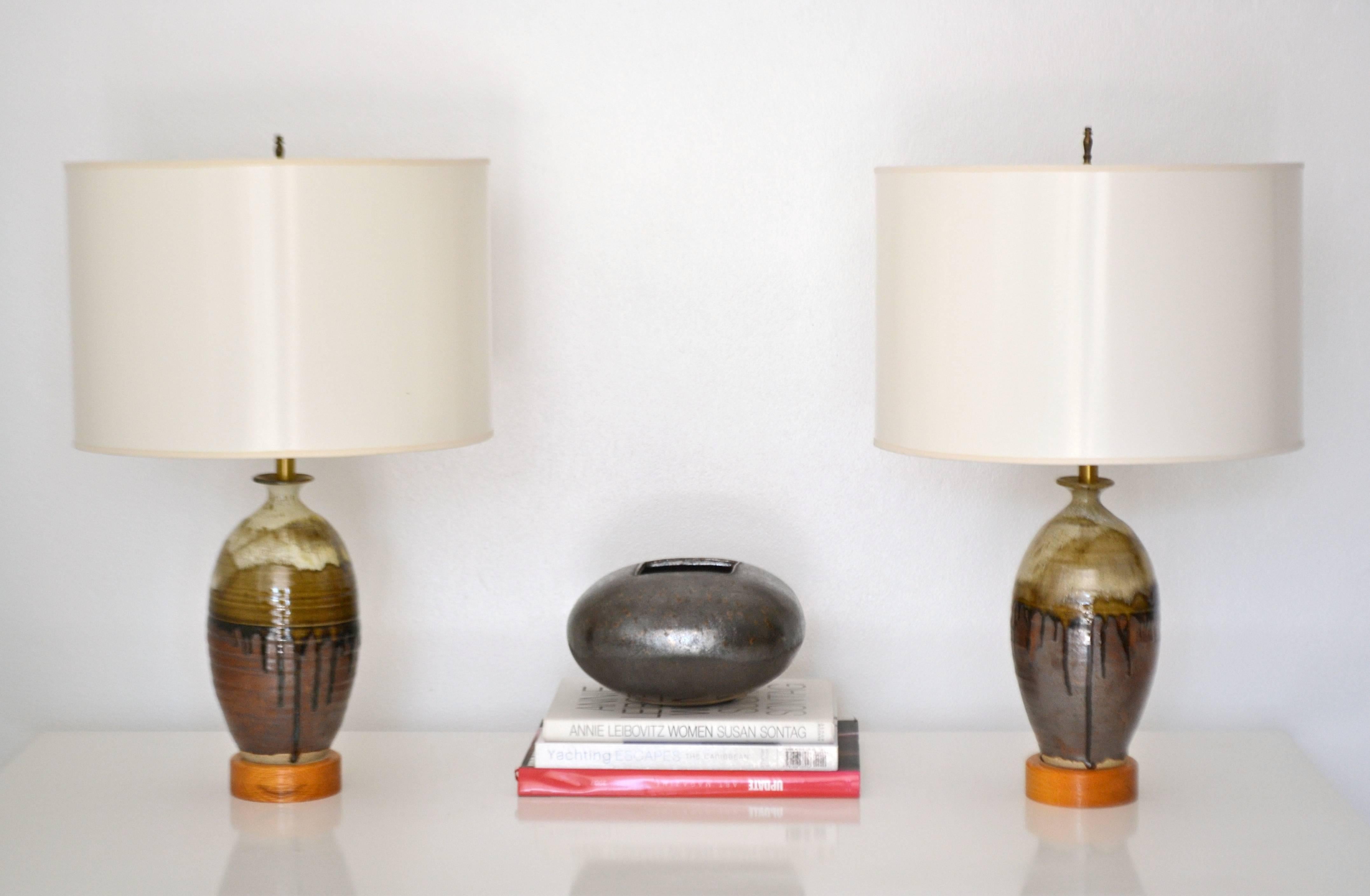 Striking pair of midcentury jar form ceramic table lamps, circa 1950s-1960s. These artisan thrown lamps are drip glazed in natural earth tones mounted in turned wood bases and wired with brass fittings. Shades not included.
Measurements: The height