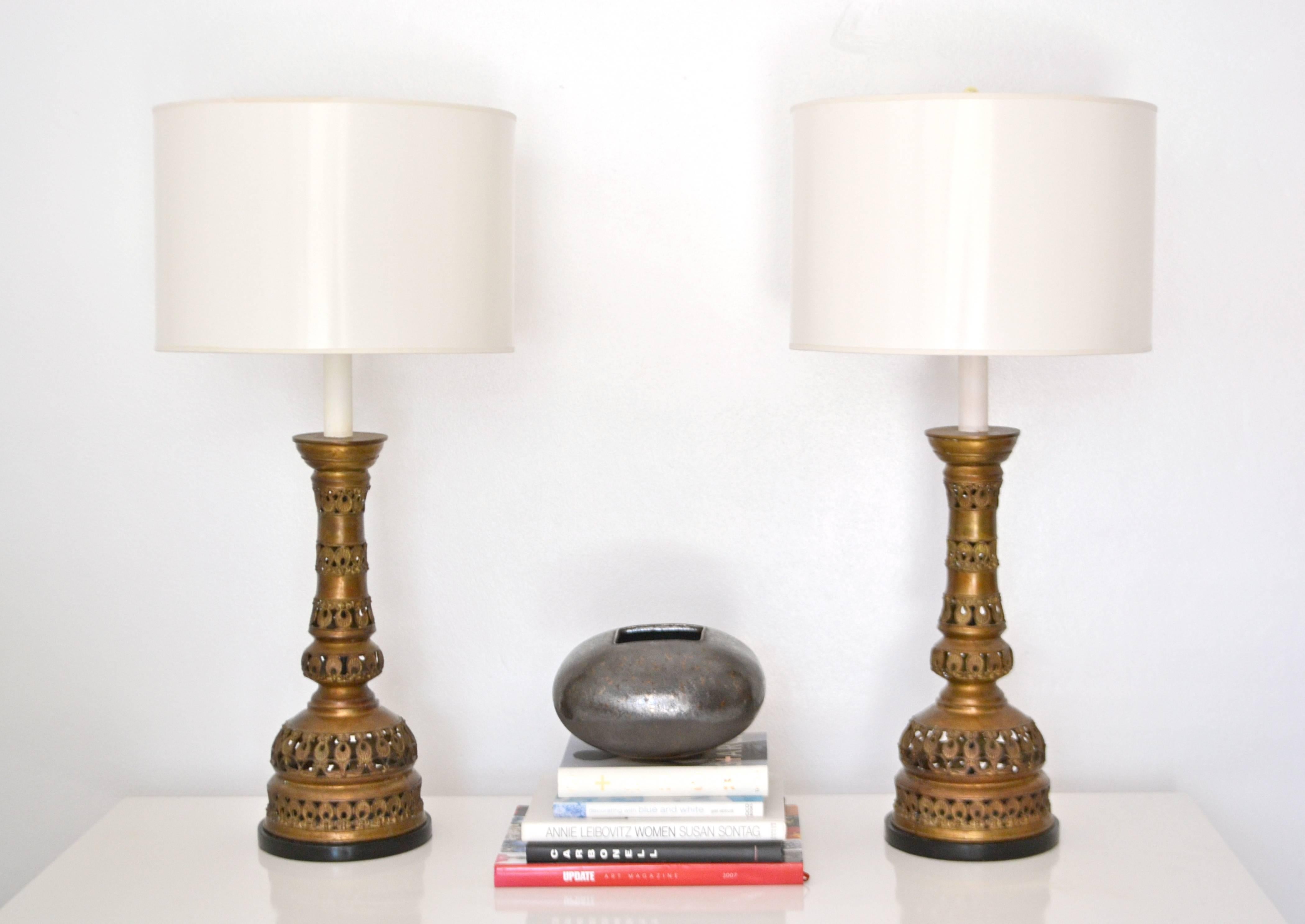 Exquisite pair of midcentury patinated brass candlestick table lamps, circa 1940s-1950s. These stunning table lamps are embellished with an open fretwork design. The brass forms are mounted on turned ebonized wood bases. Shades not