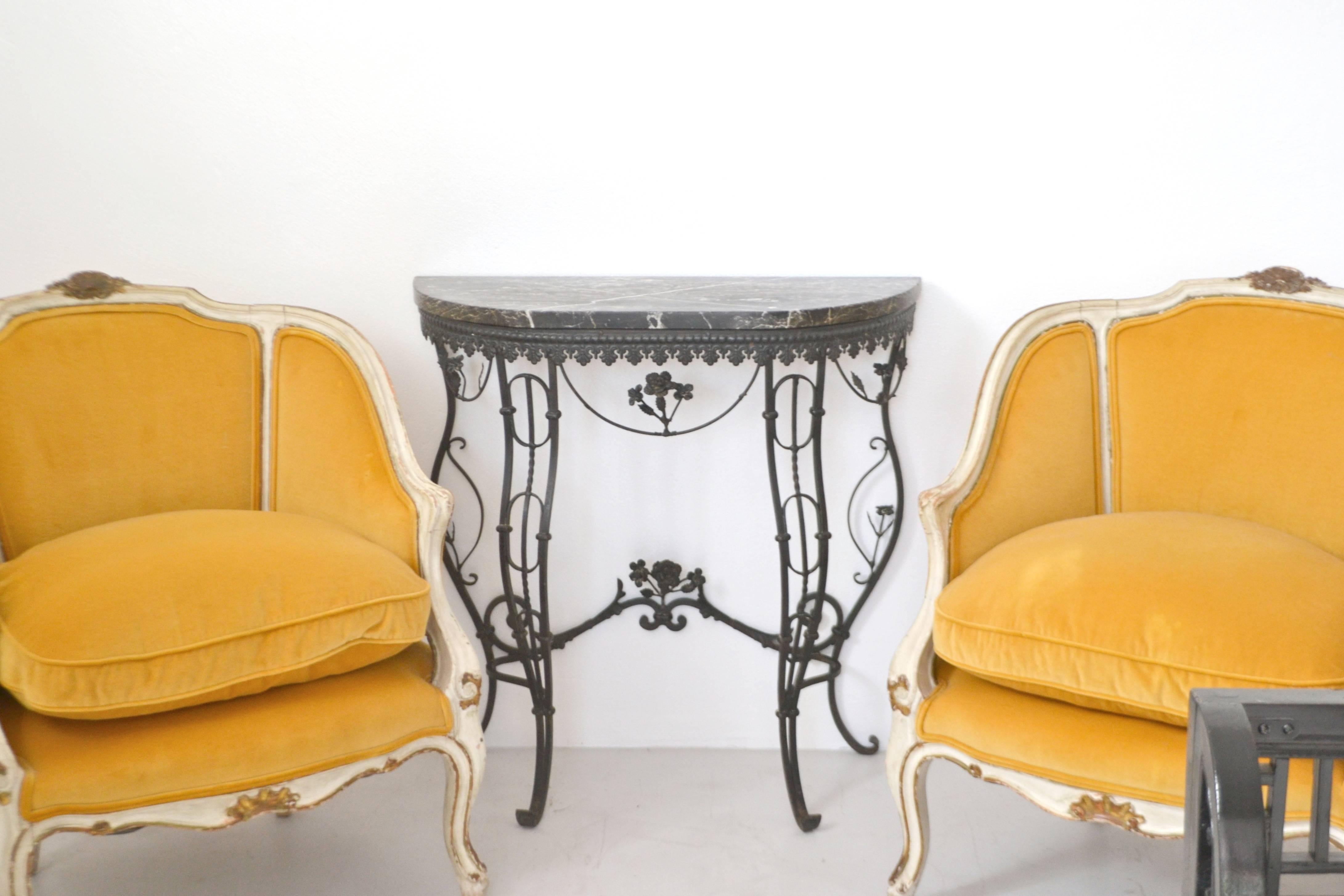 Glamorous pair of French Louis XV style bergere chairs, circa 1920s. These stunning artisan crafted white painted wood framed chairs with giltwood accents and down cushions. The armchairs are upholstered in the original lemon drop yellow cotton