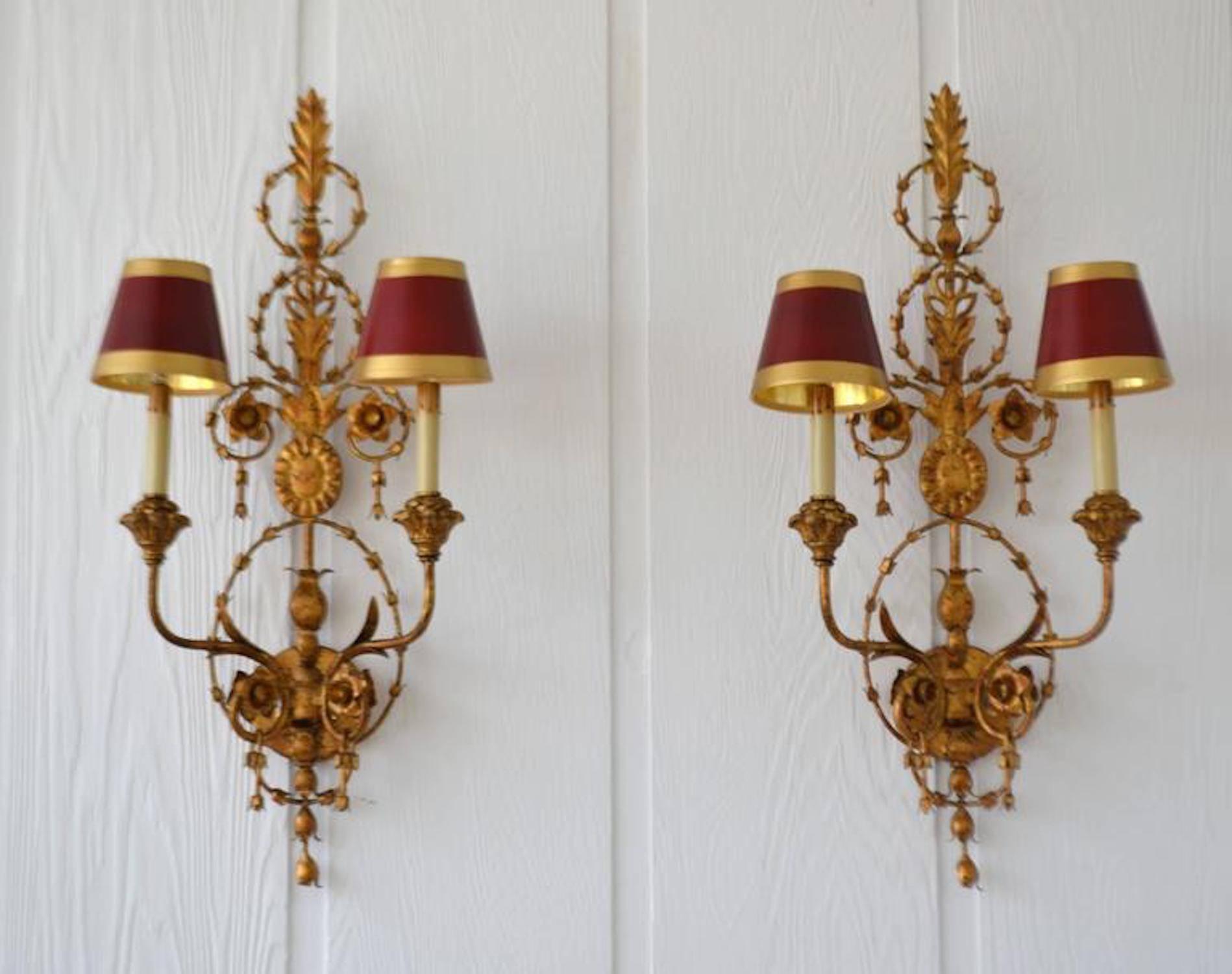 Stunning pair of Italian neoclassical style hand-wrought gilt metal two-arm sconces, circa 1950s-1960s. These stunning decorative two-light sconces are designed with hand-carved giltwood accents and parchment paper shades.