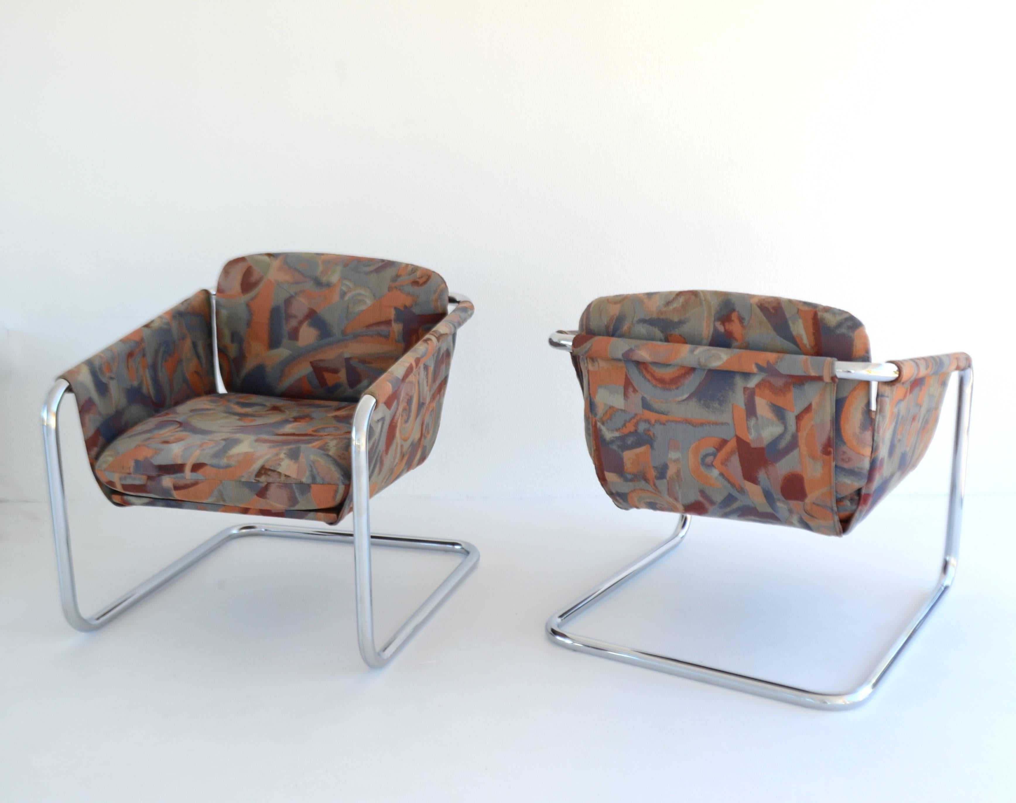 Striking pair of postmodern cantilevered chromed steel sling form lounge chairs, circa 1970s-1980s. These stunning club chairs are upholstered in their original Pop Art patterned fabric which could be reupholstered, mounted on sleek polished chrome