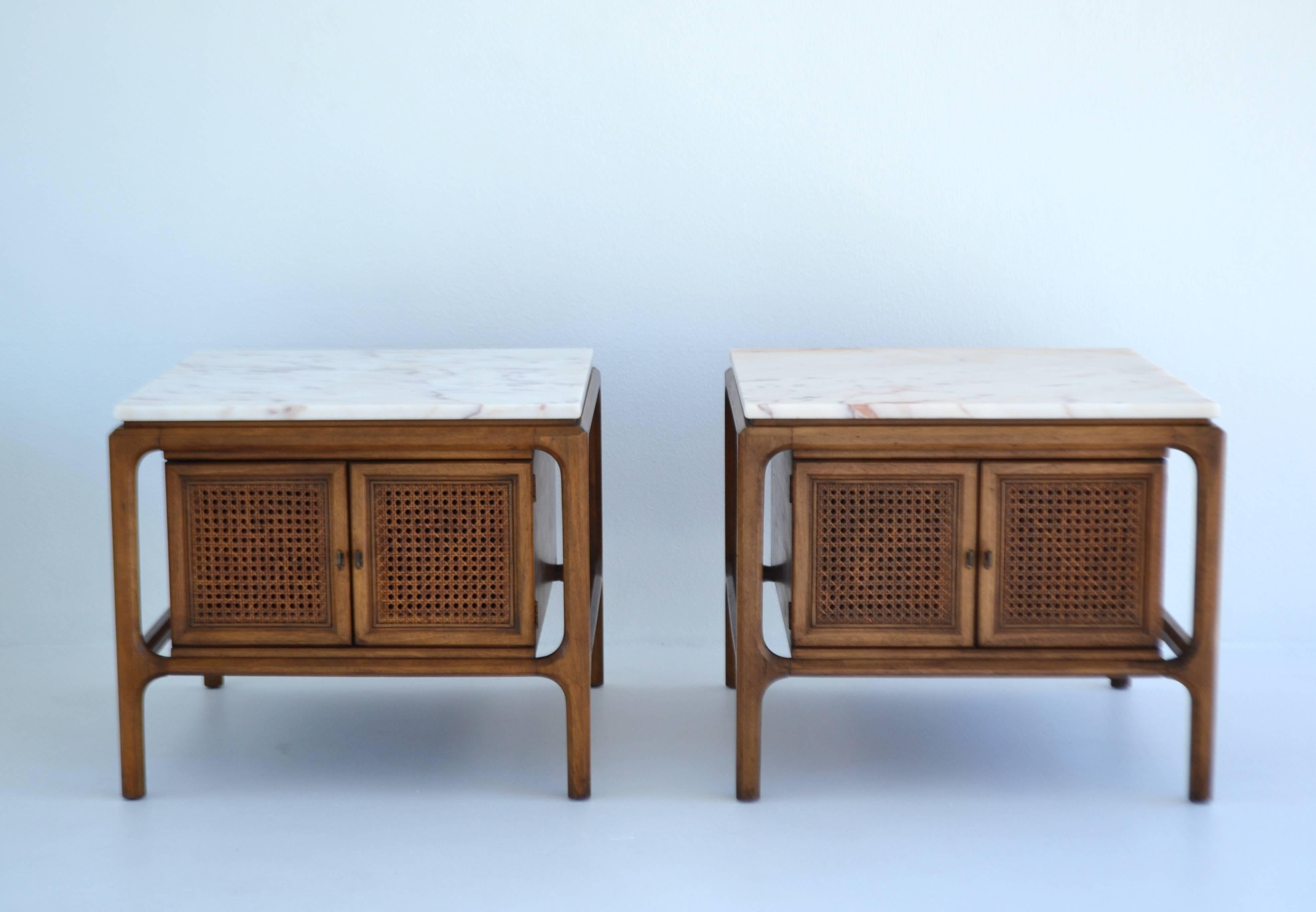 Striking pair of Midcentury sculptural walnut end tables or cabinets, circa 1950s-1960s. These beautiful handcrafted bedside tables or nightstands are artisan designed of carved walnut, caned door fronts, aged brass door pulls and honed white