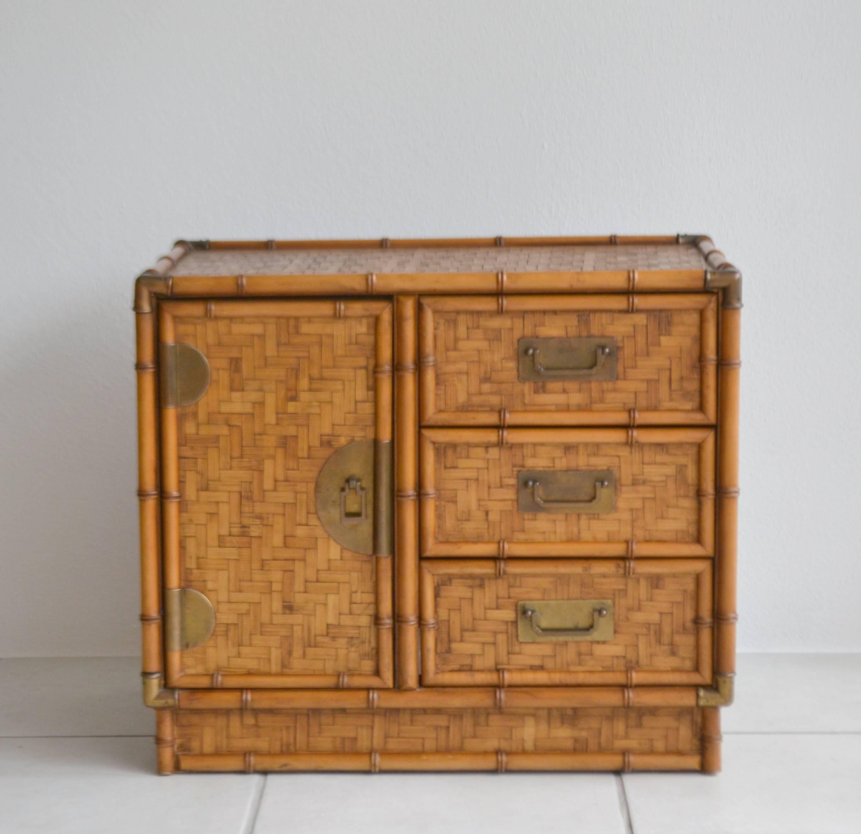 Striking pair of Mid-Century woven reed nightstands or side cabinets, circa 1960s. These stunning side tables or end tables have been artisan crafted in the form of Campaign style chests with faux bamboo detailing and accented with patinated brass