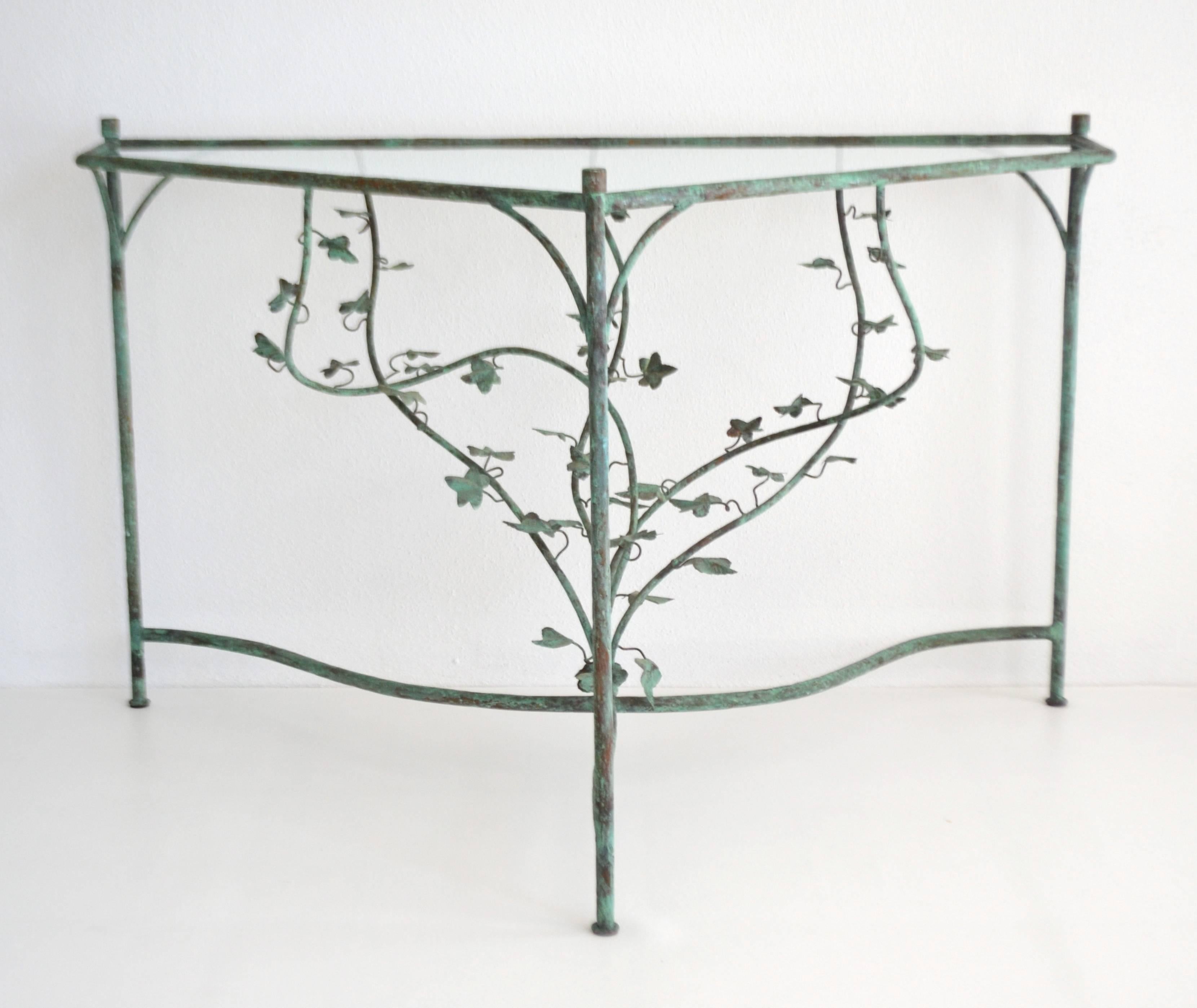 Glamorous Hollywood Regency style handwrought triangular form console table or center hall table, circa 1950s. This striking hammered copper corner table with aged verdigris oxidized patina is designed with exquisite scrolling vine form details and