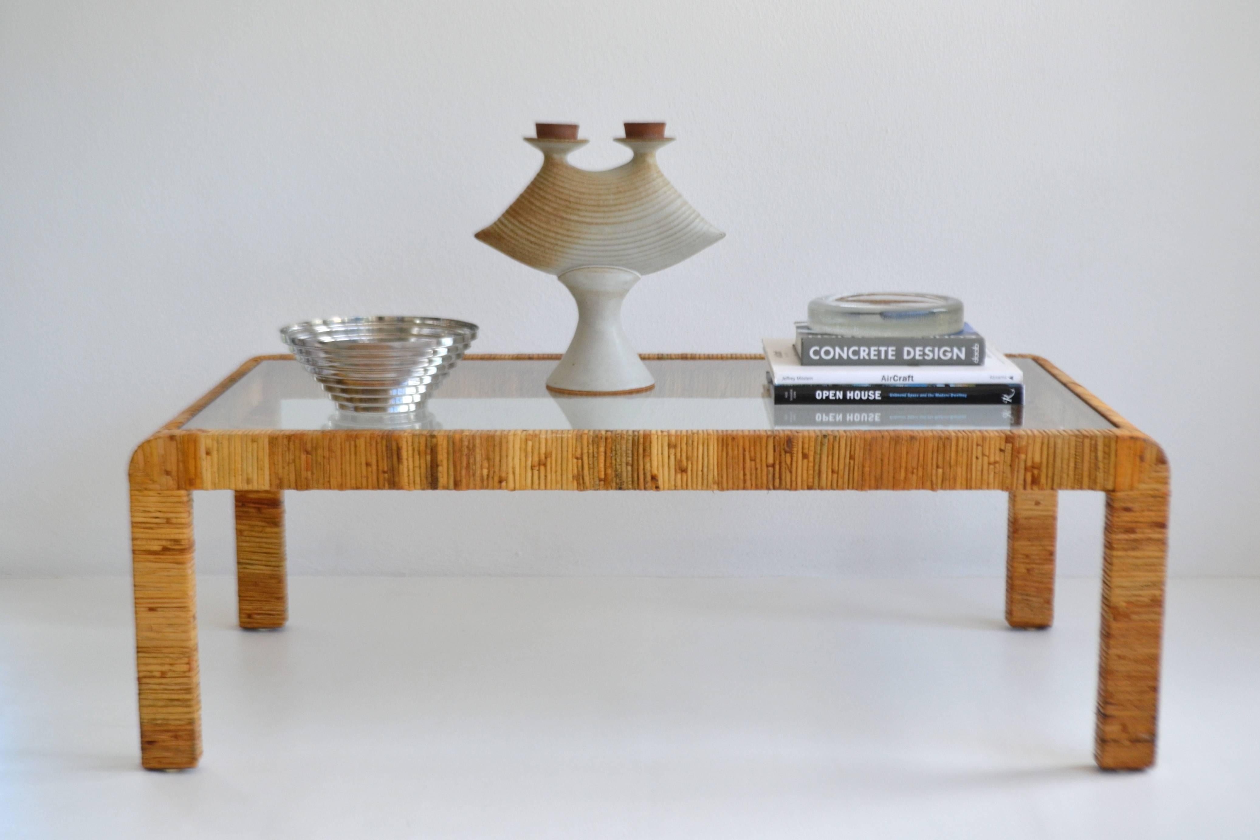 Striking Mid-Century rattan cocktail table, circa 1960s-1970s. This sleek rattan wrapped hardwood coffee table of waterfall edge design is accented with an inset glass top.