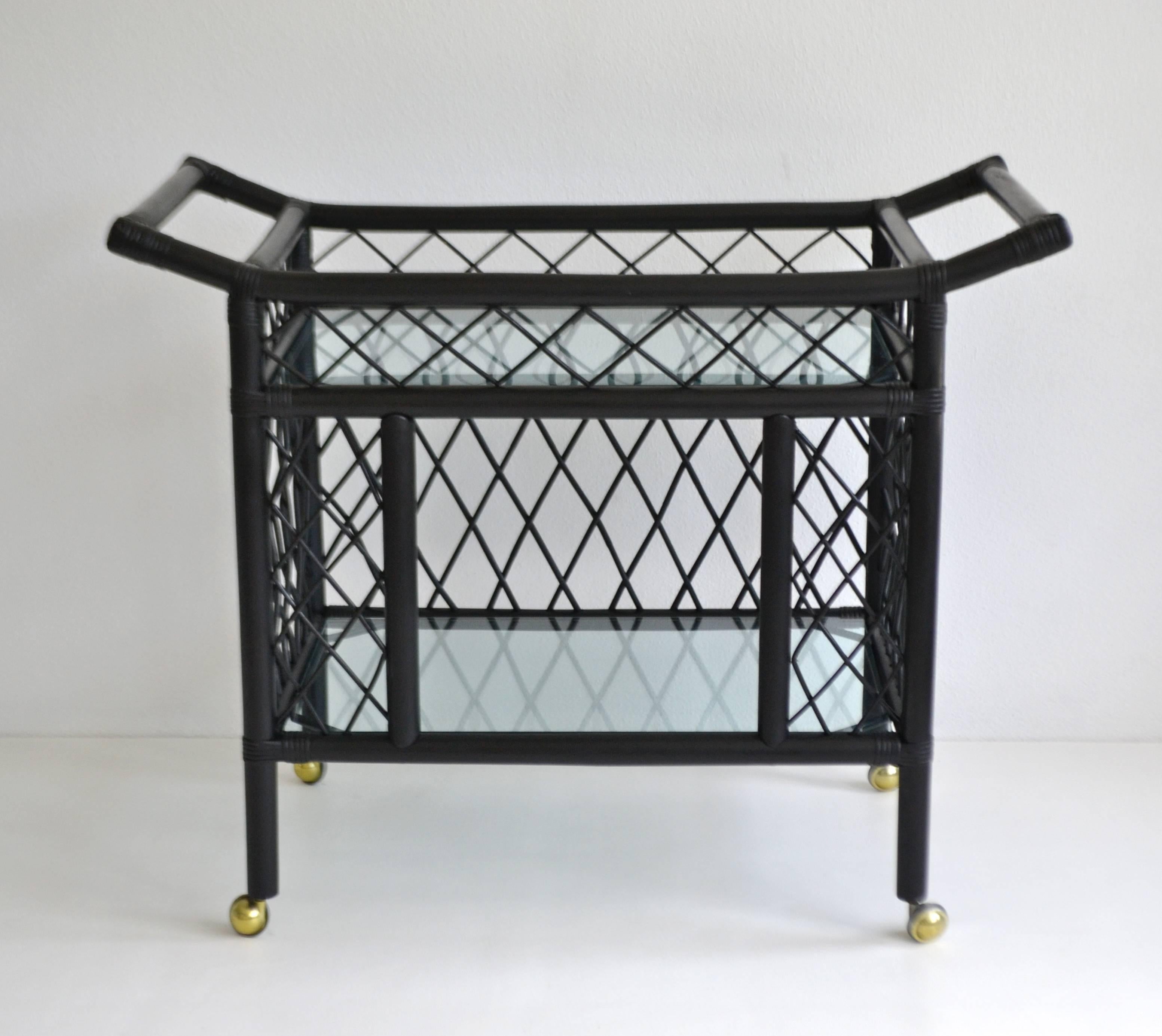 Glamorous midcentury black lacquered bamboo bar cart, circa 1960s. This stunning sculptural two-tier bar cart / sideboard is designed with an open woven reed fretwork pattern. The exquisitely crafted serving cart is outfitted with two large inset
