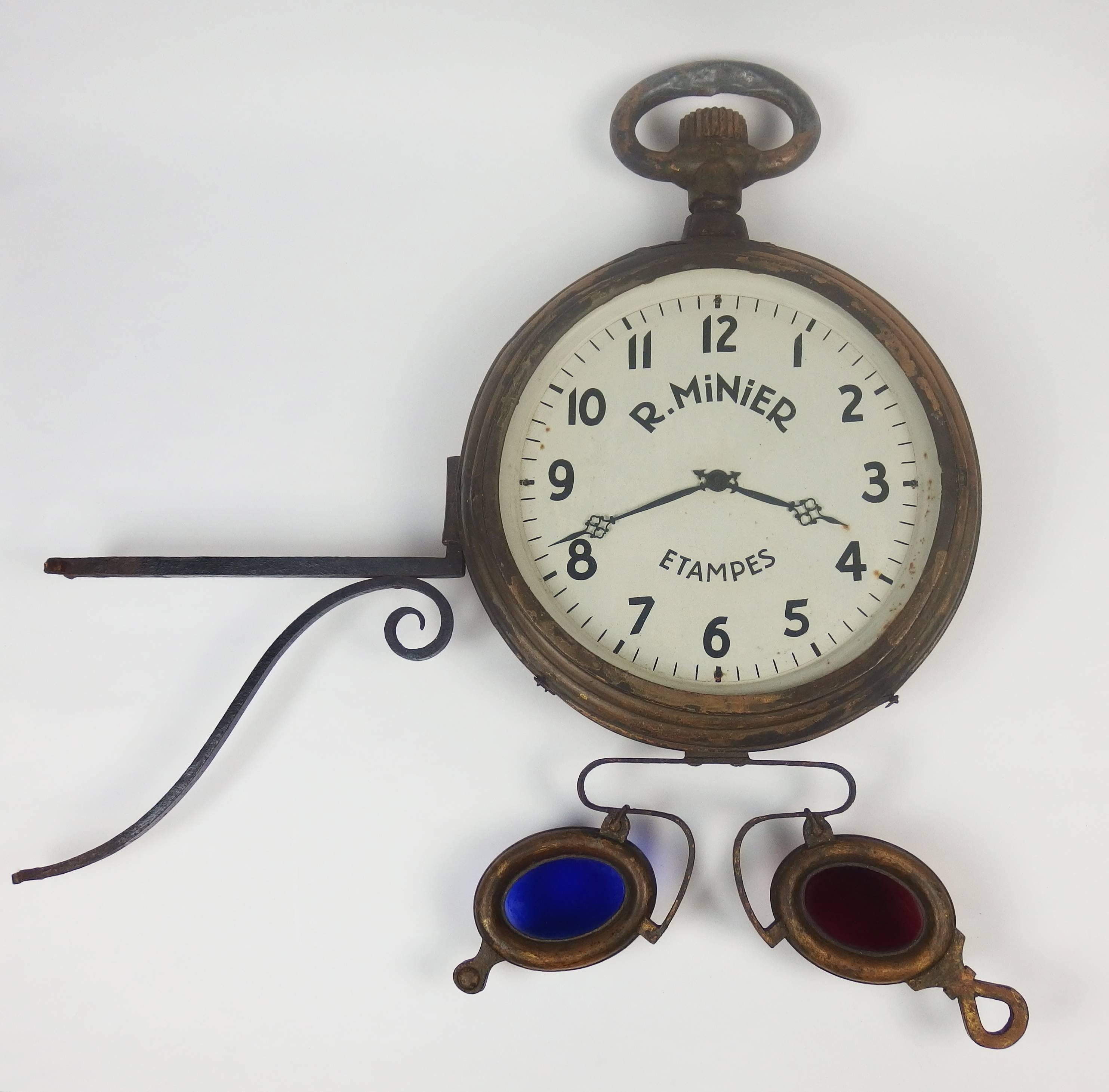 This zinc sign is double. It presents a clock and spectacles.
The spectacles are in gilt zinc with blue and red glasses.
The watch is also in gilt zinc, the faces of this watch were repainted in the 1930s in order to change the name of the