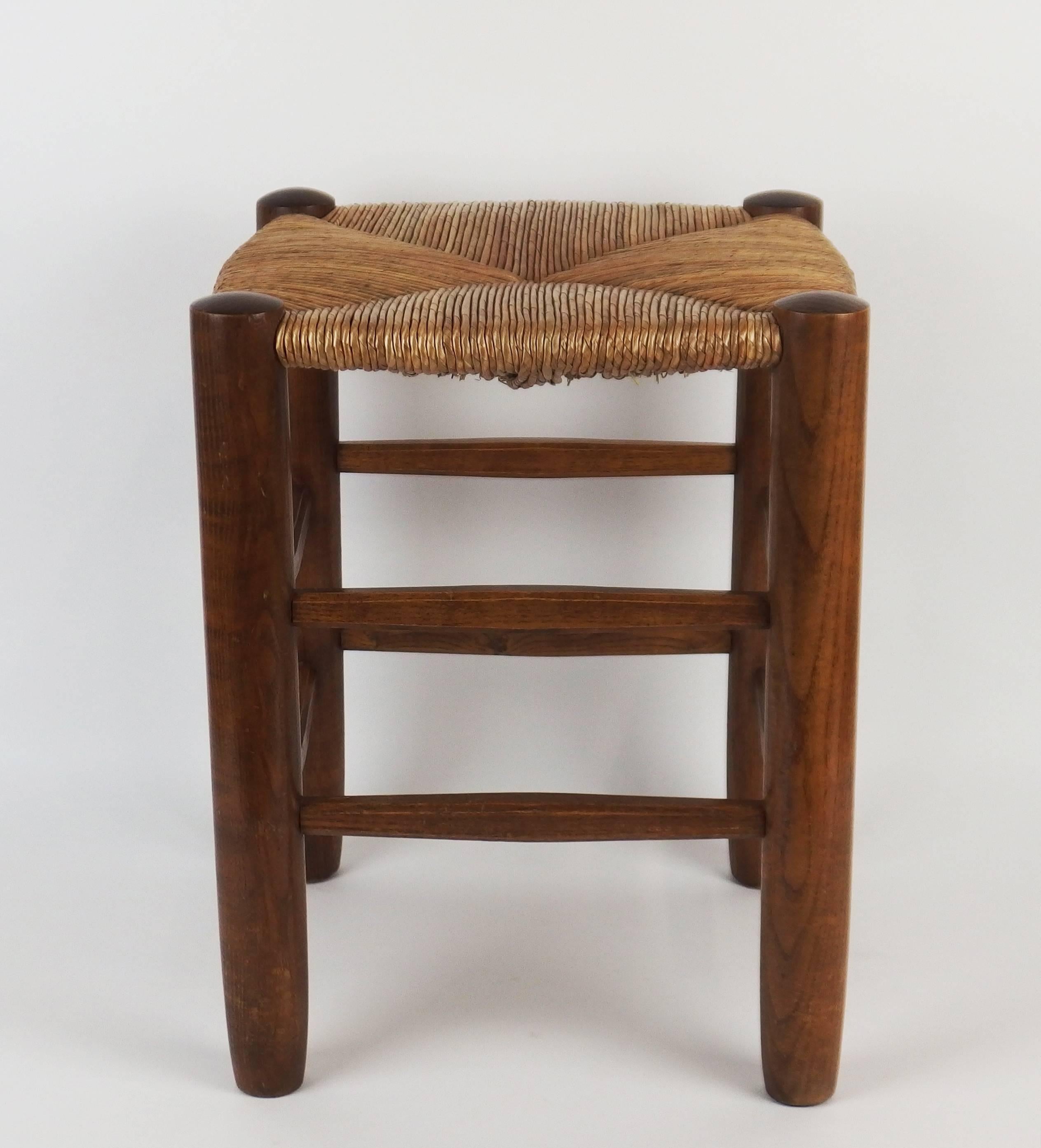 A brown tinted ash stool with a woven rush seat designed by Charlotte Perriand.
Charlotte Perriand used this type of stool in several interior designs among them houses in Issoire and flats in Meribel.
 