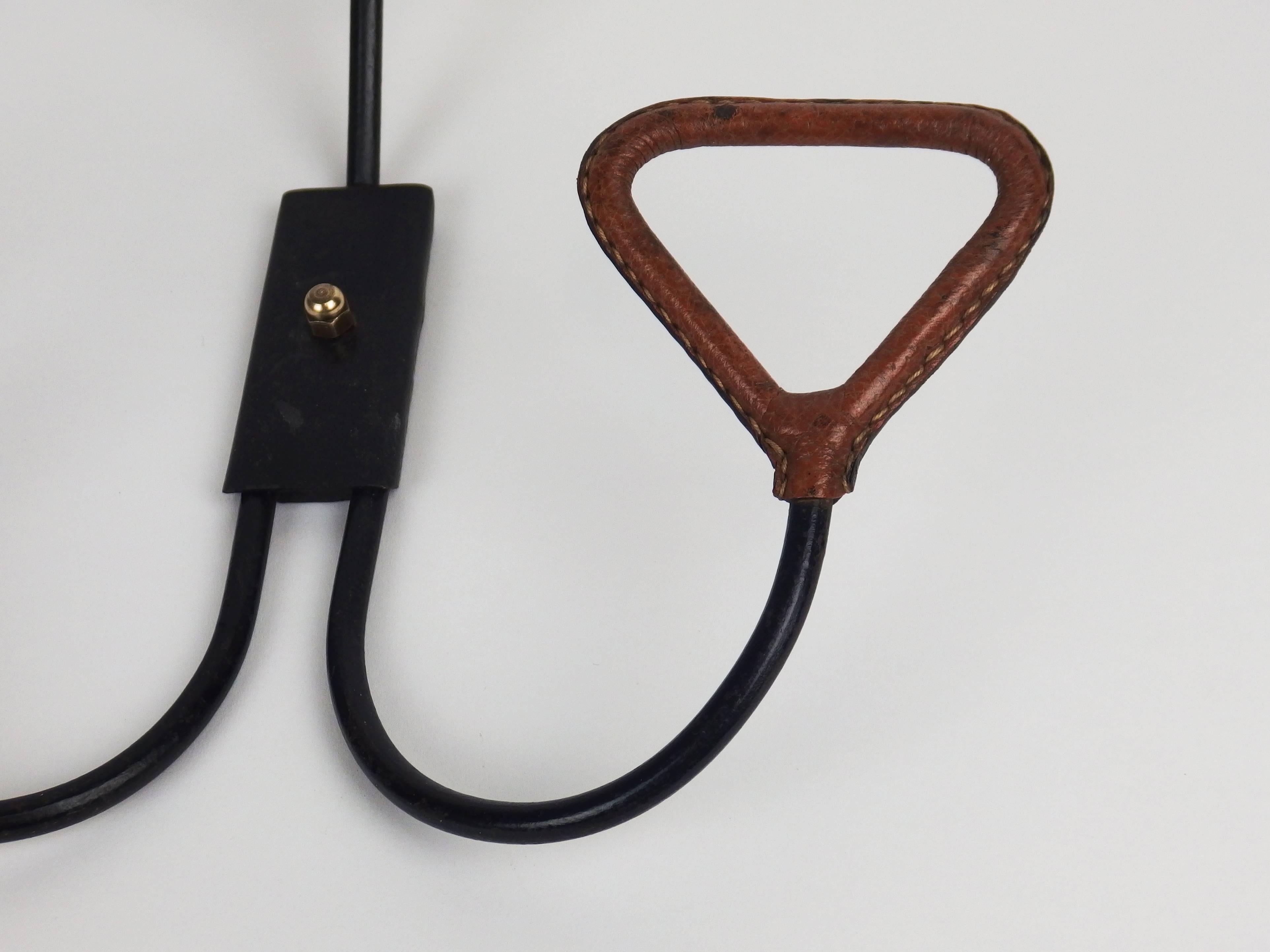 A coat rack with three brown stitch leather hooks on a black enameled iron frame. This type of coat rack is sometimes presented as designed by Jacques Adnet.