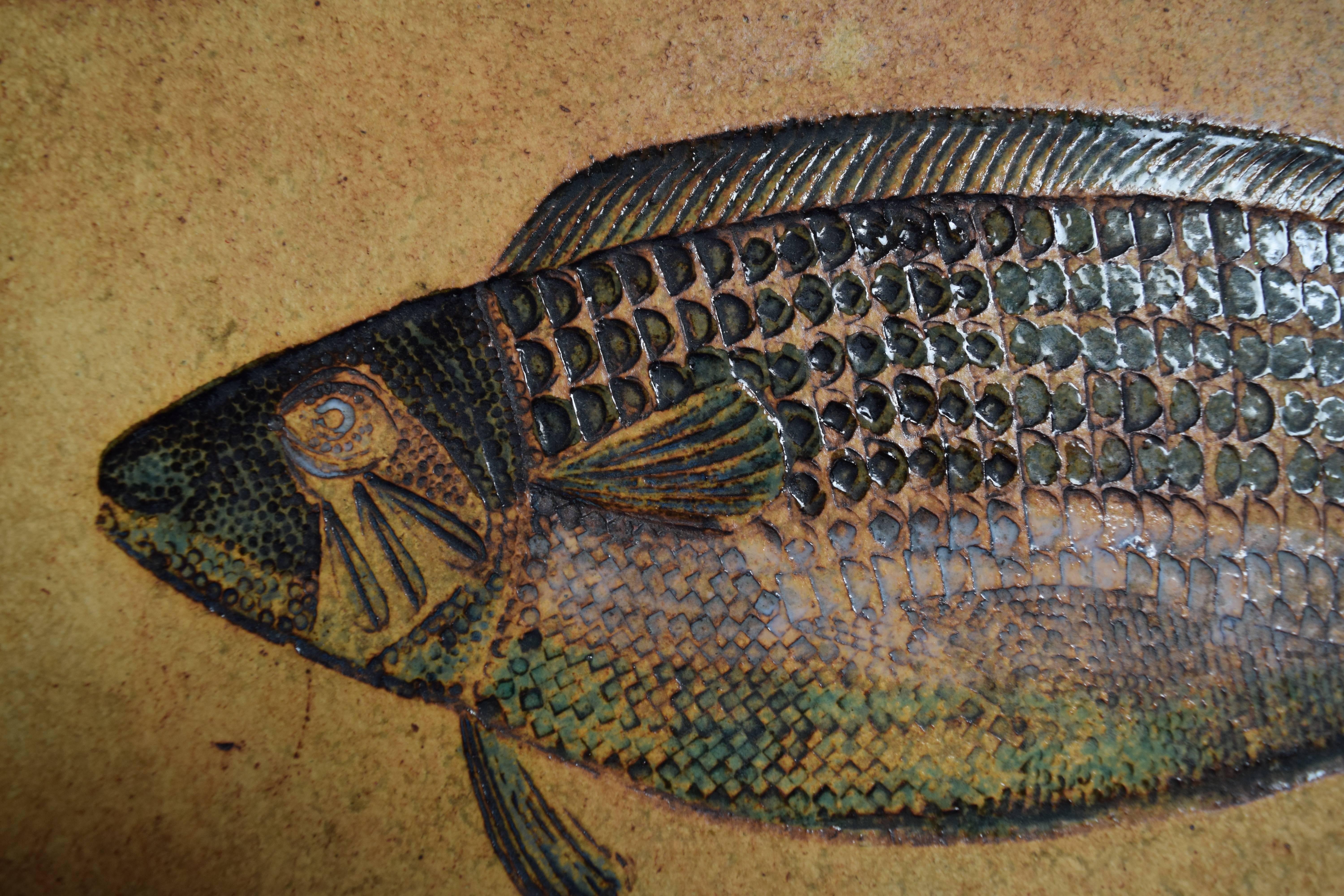 Spectacular and large ceramic tile evocative of a prehistoric fossil fish, executed in intricate, dimensional detail and finished in a shimmering range of blues and greens. Signed 