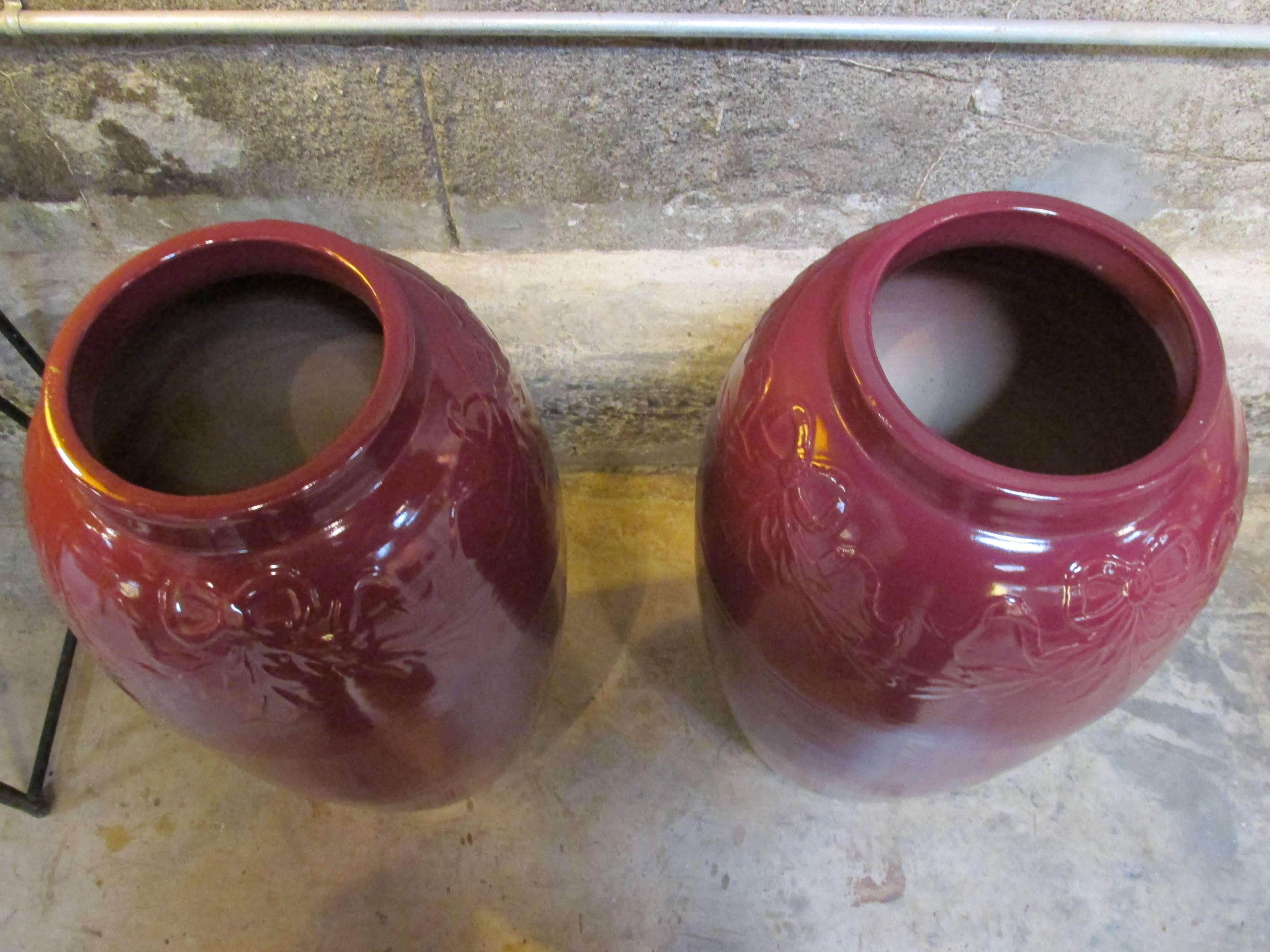 A matched pair of large-scale Mid-Century Modern pottery floor pots or oil jars with a garland and ribbon relief design. Excellent original condition. Beautiful addition to your garden, but may be enjoyed as an interior or exterior decorative