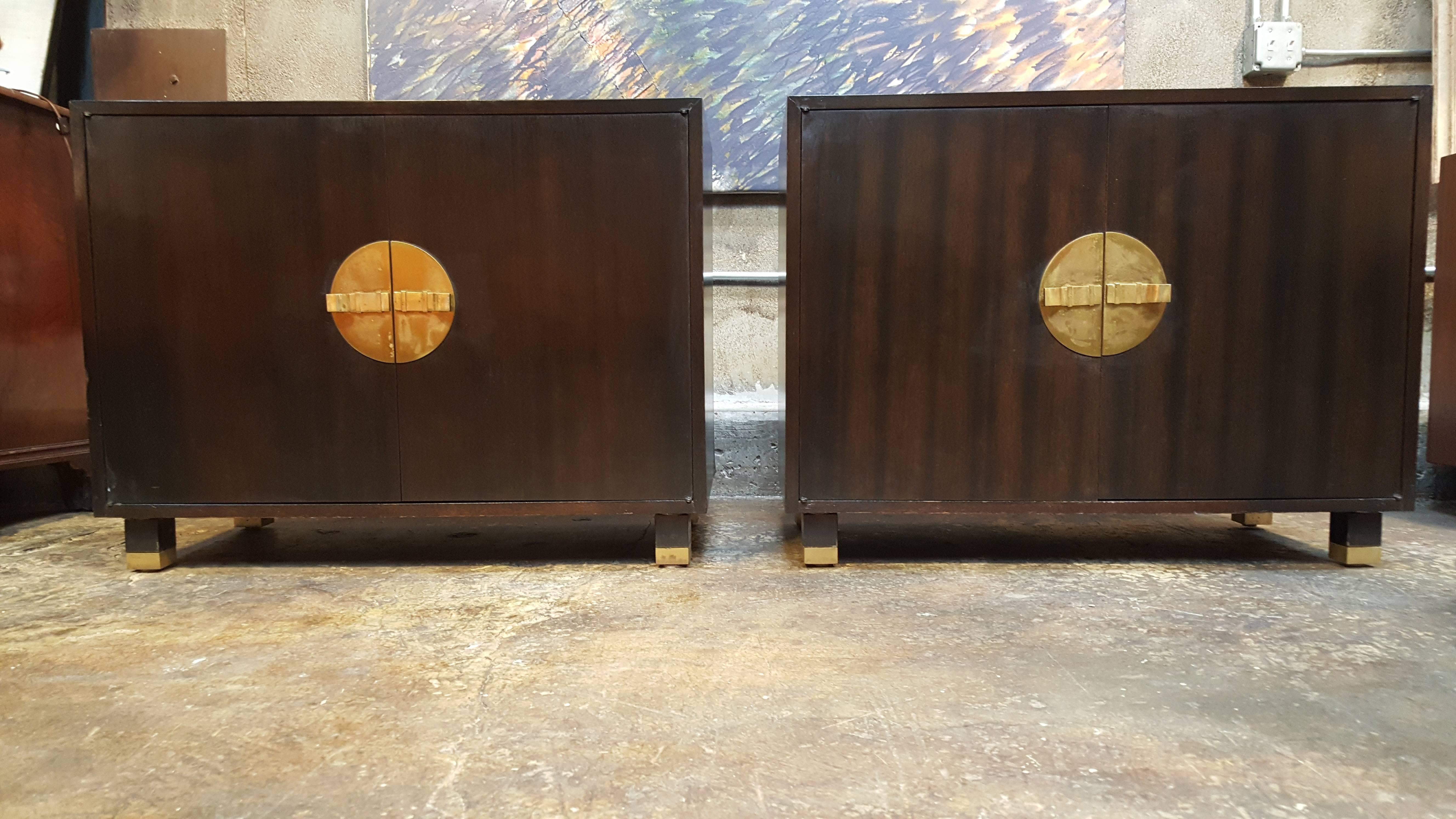 A pair of Mid-Century cabinets with impressive brass hardware and brass detail to rectangular feet. Double doors open to ample storage. May be enjoyed as end tables, nightstands or small credenzas. Original finish, circa. 1950s.