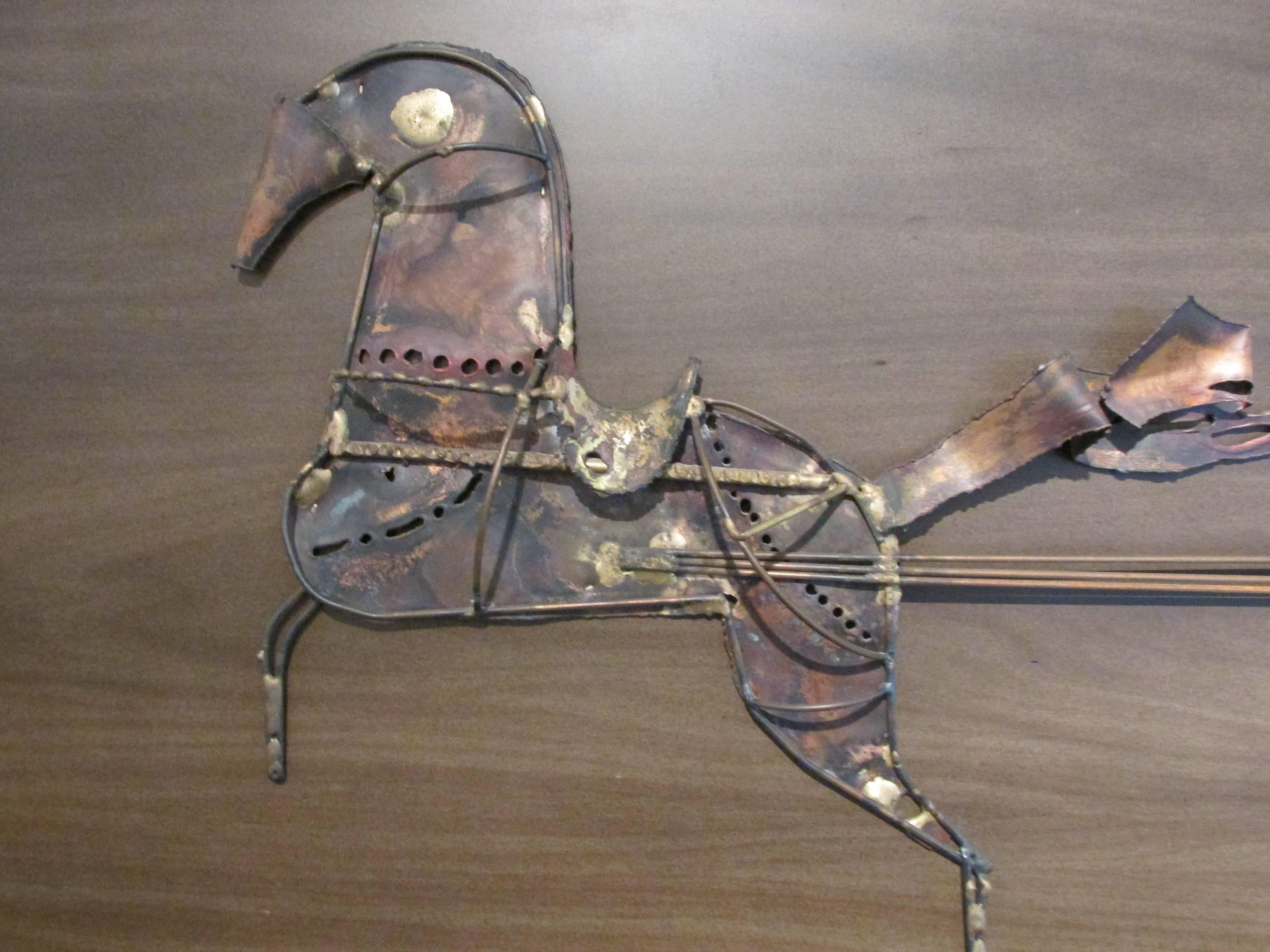 A torch-cut brass and copper wall sculpture mounted to a framed wooden back-plate. Made primarily in copper with some brass and steel components. Depicting a horse, chariot and shield, circa 1970s. Style of Curtis Jere. Large scale wall sculpture