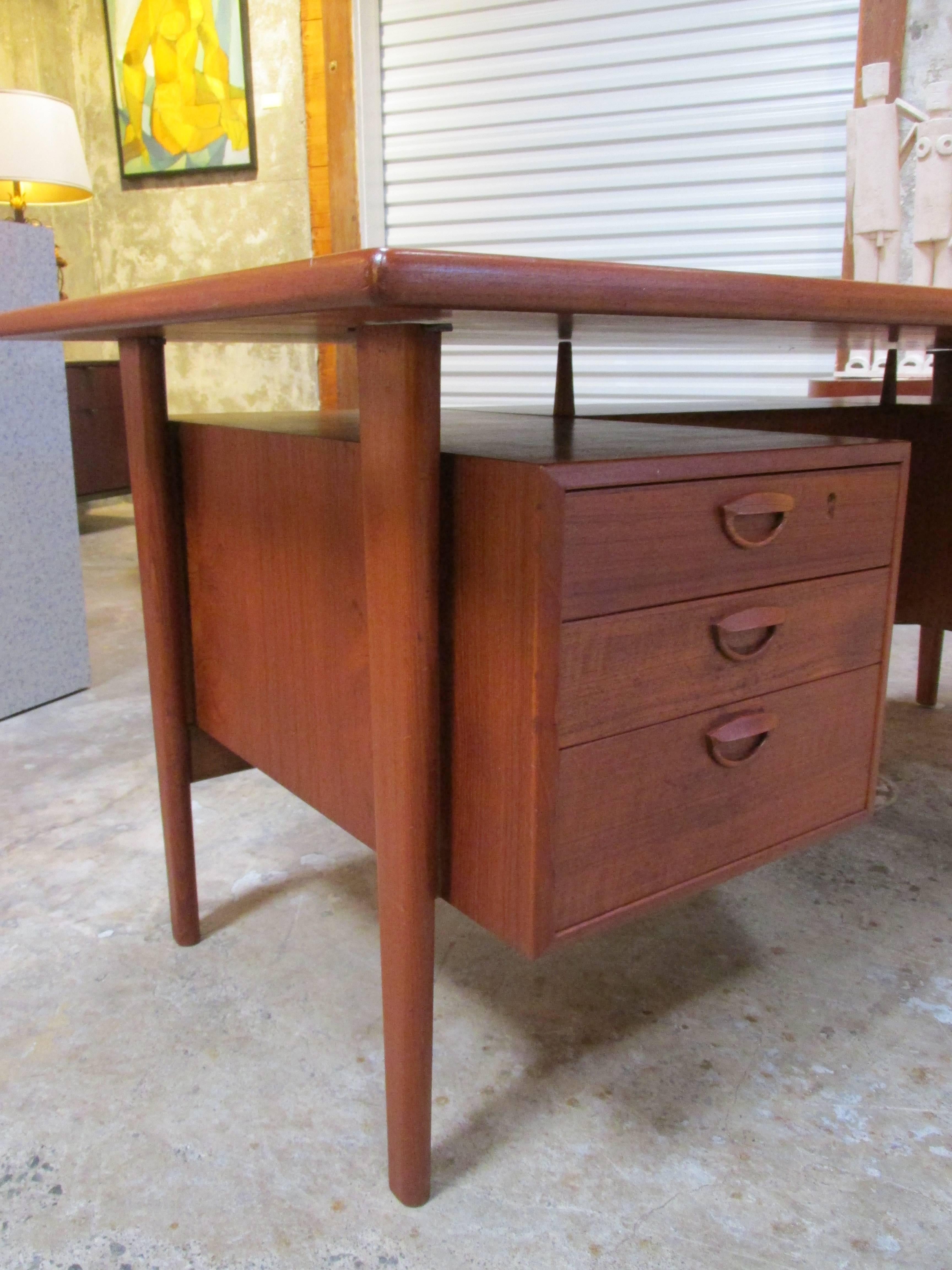 Iconic and classic teak executive desk designed by Kai Kristiansen, circa 1960. Features a floating top design with six drawers at front of desk and two locking storage cabinets with additional open storage at back of desk. Includes two original