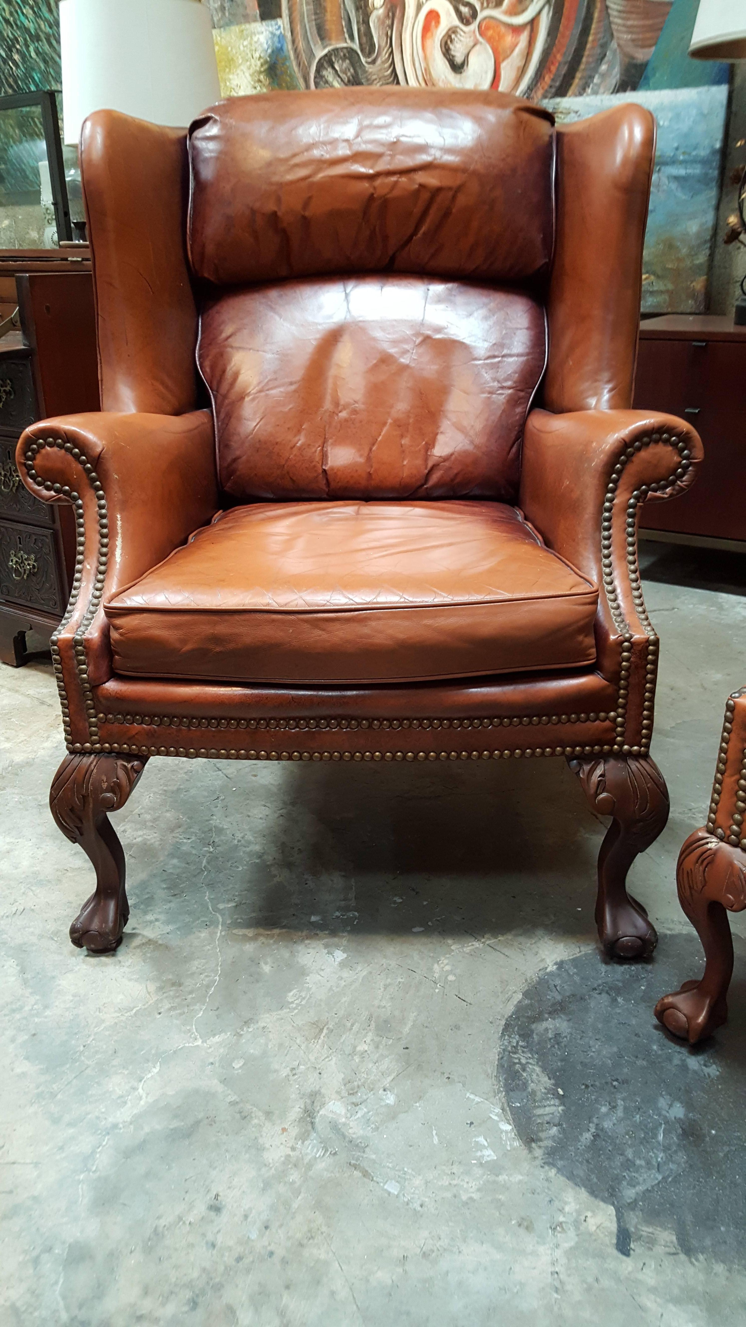 A pair of 20th century leather wing chairs by Schafer Brothers Furniture. Classic carved ball and claw leg and brass nail-head detail. High grade leather with fading and wear, retaining excellent structural integrity. A very comfortable and handsome