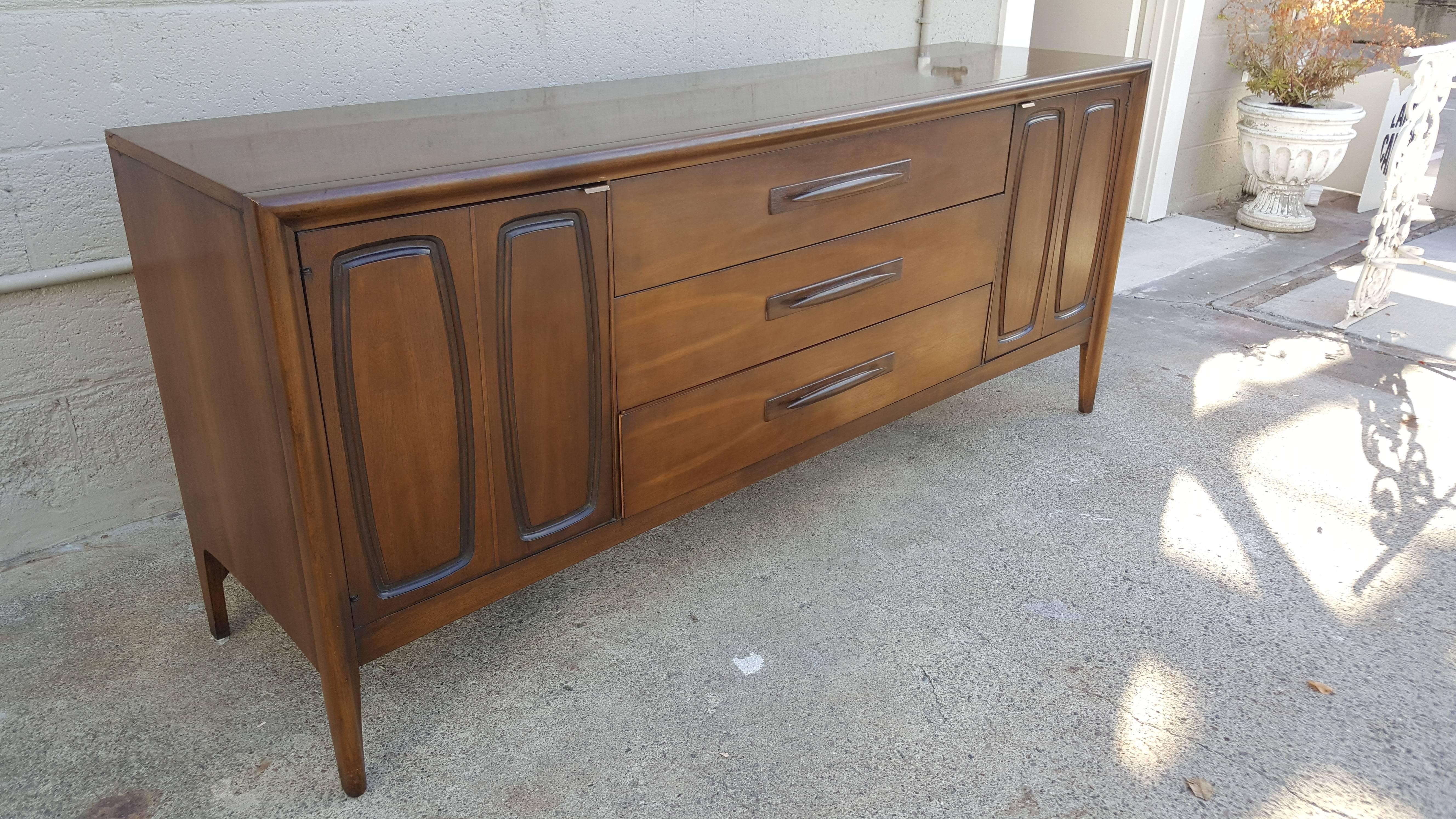 A mid-20th century modern walnut credenza manufactured by Broyhill Furniture, circa 1960. Long and sleek measuring 6 feet wide. Ample storage with nine drawers and six behind cabinet doors. Solid oak secondary woods and steel drawer glides. Broyhill