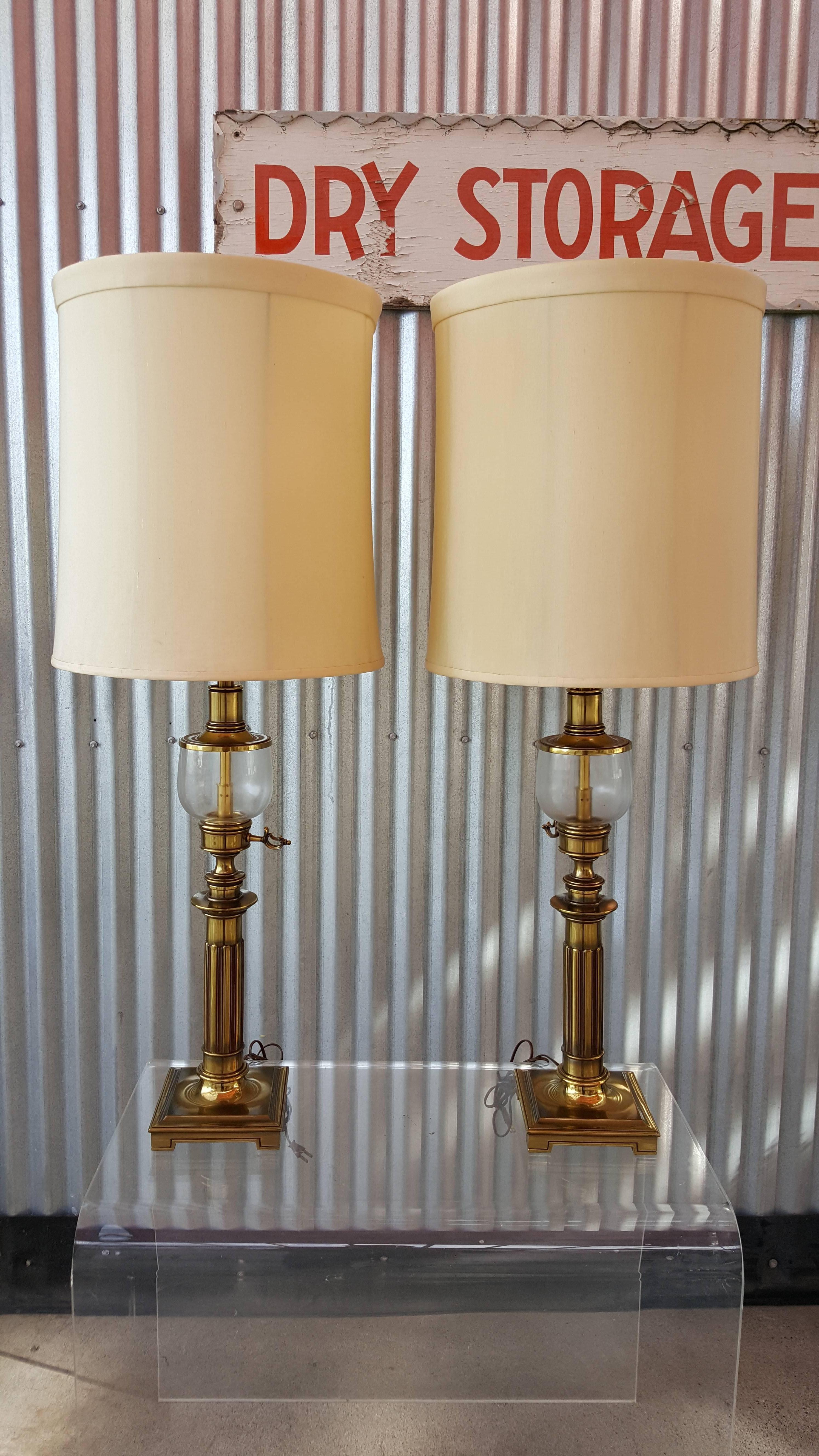 A large-scale pair of solid polished brass lamps in a Federal style oil lamp design. Ribbed column over a square base with a glass detail. Lamps are available with or without original shades, just pay additional shipping for silk shades. Detailed,