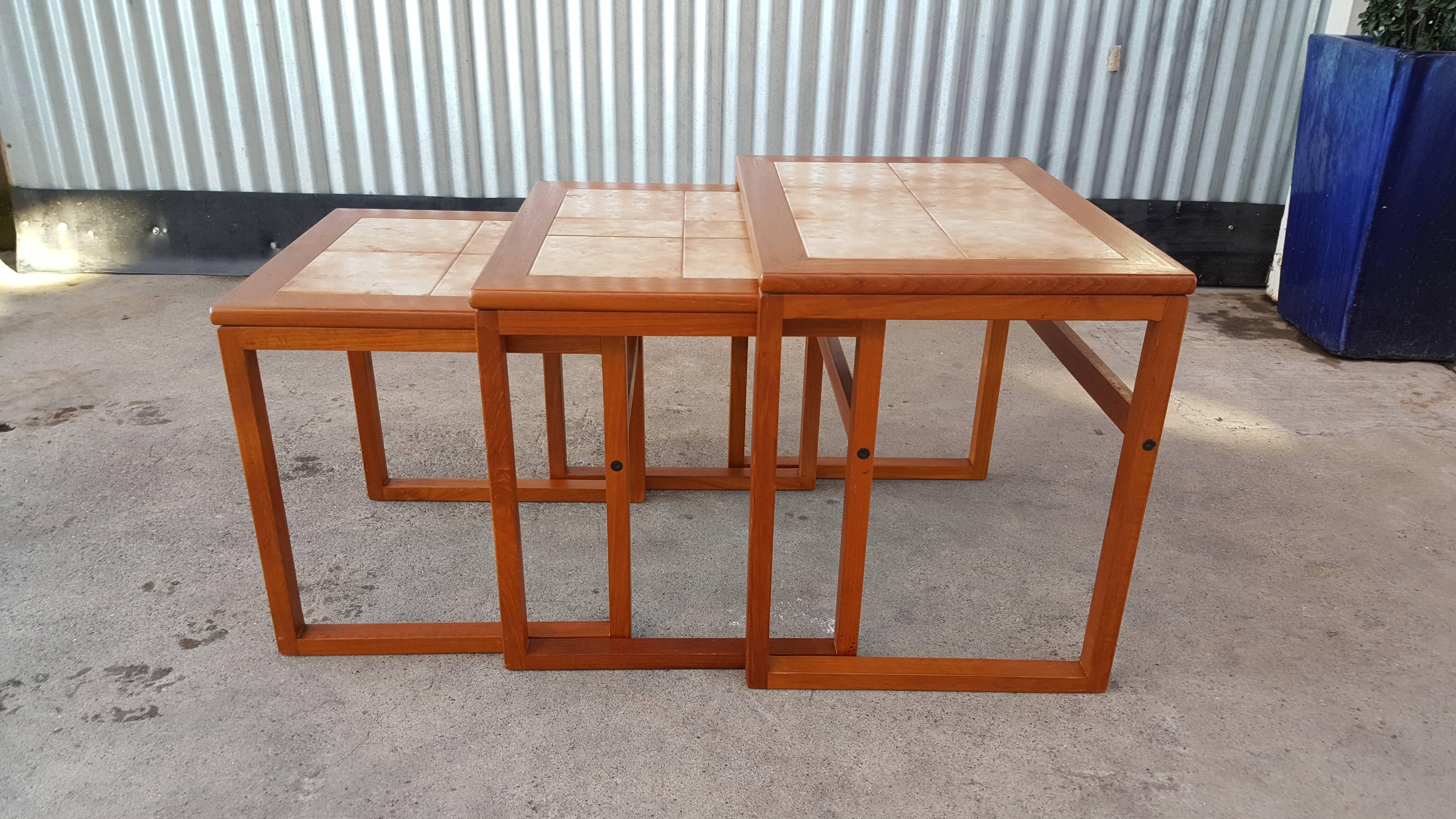 A set of three teak end tables with ceramic tile tops. May nest together to conserve space or be enjoyed as three separate end tables. Smaller tables measure 17.5