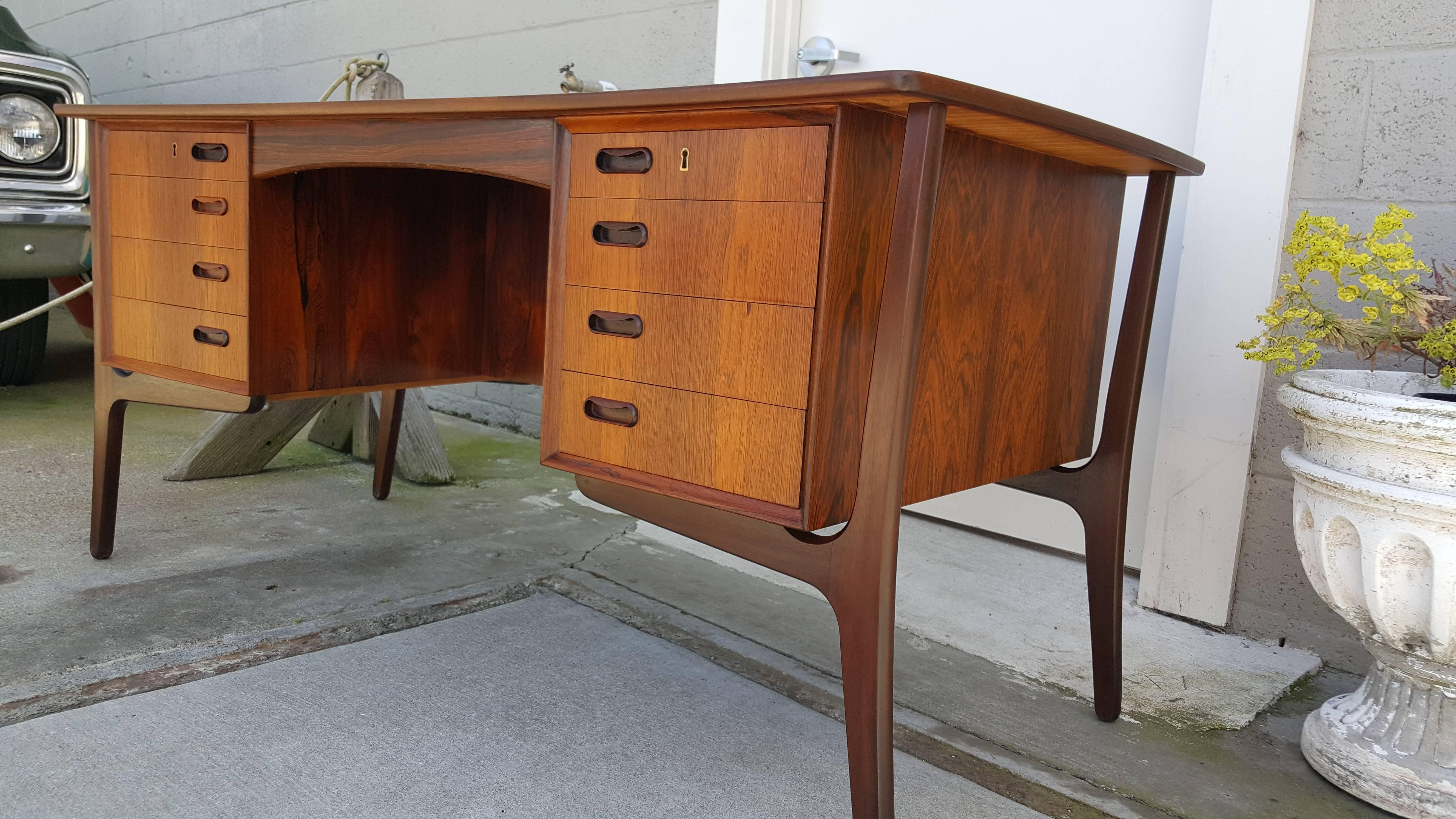 Danish Modern rosewood desk with a curved top floating on an exoskeleton frame. Eight drawers with a finished back featuring a locking cabinet door and a bookshelf. Key included. Nice original finish in very good vintage condition.