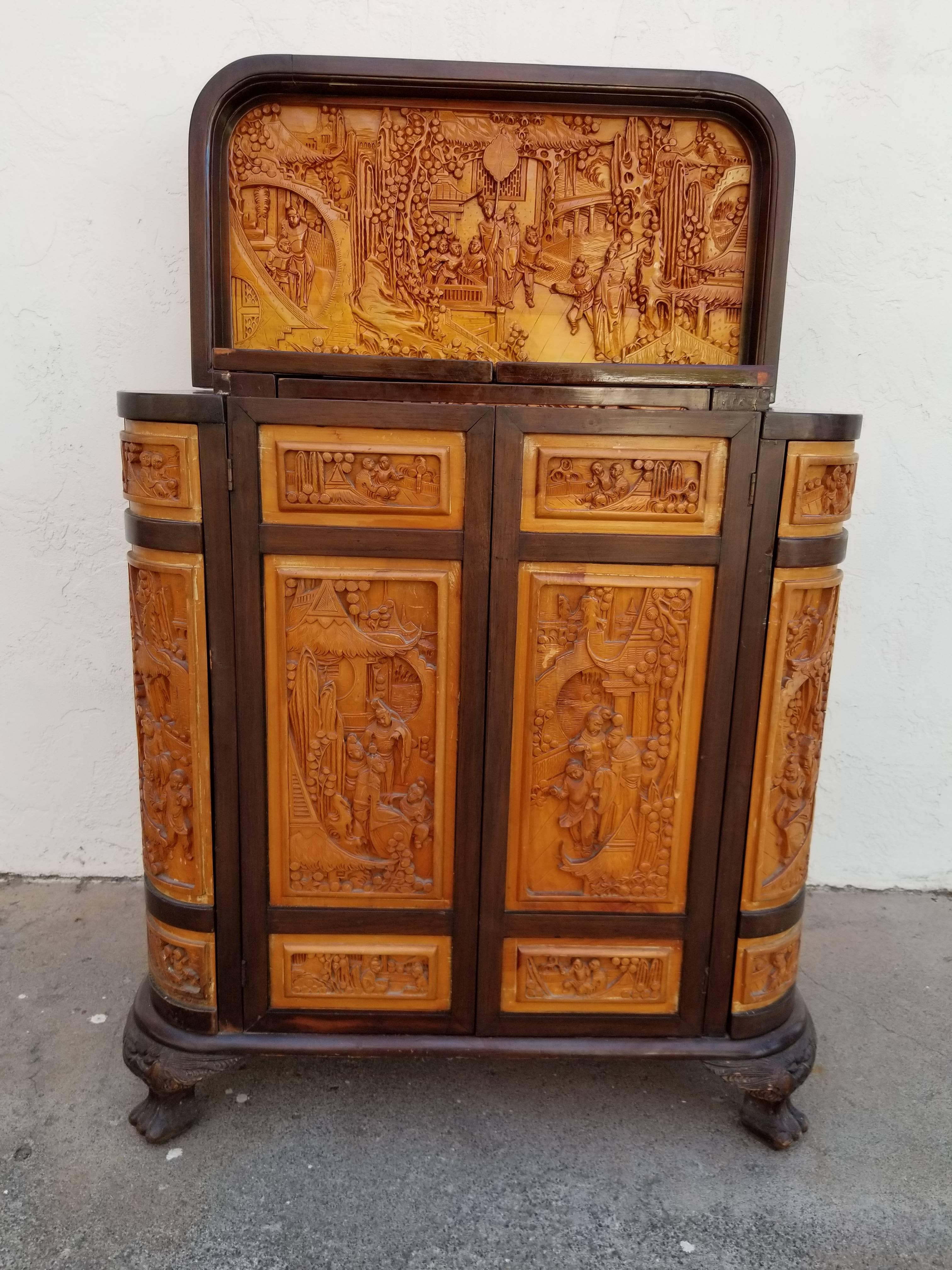 Highly detailed compartmentalized flip-top dry bar with a two-tone finish. Diminutive size with cabinet doors and drawers on three sides for maximum storage. Hand-carved Asian figures, flowers and architecture. Overall height when top is open