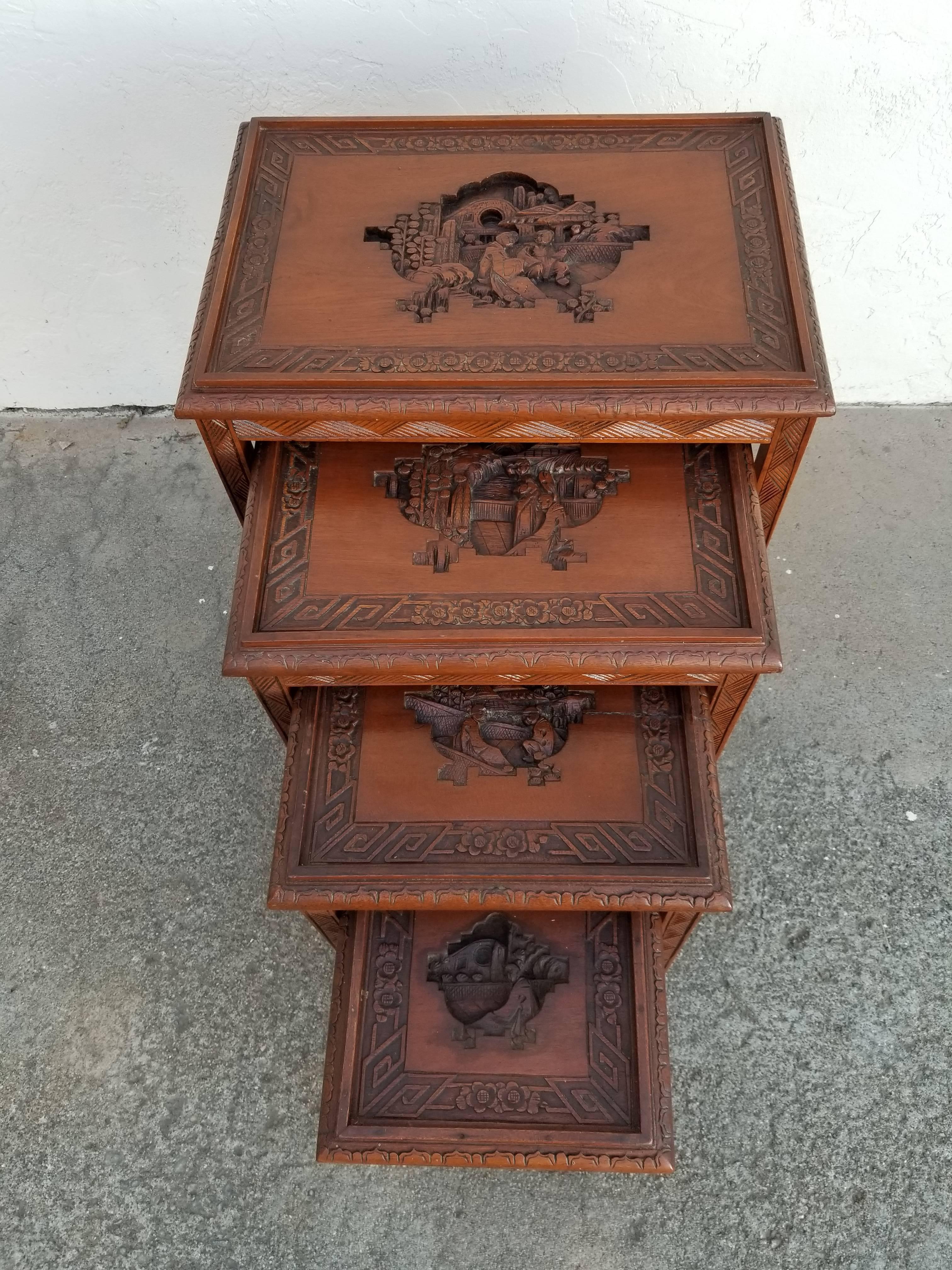 A set of four hand-carved nesting end tables made in China, mid-20th century. Nice detail to aprons and legs with carved figures and intricate borders. Smallest drawer has spring loaded hidden drawer. Very nice original condition. Smallest three