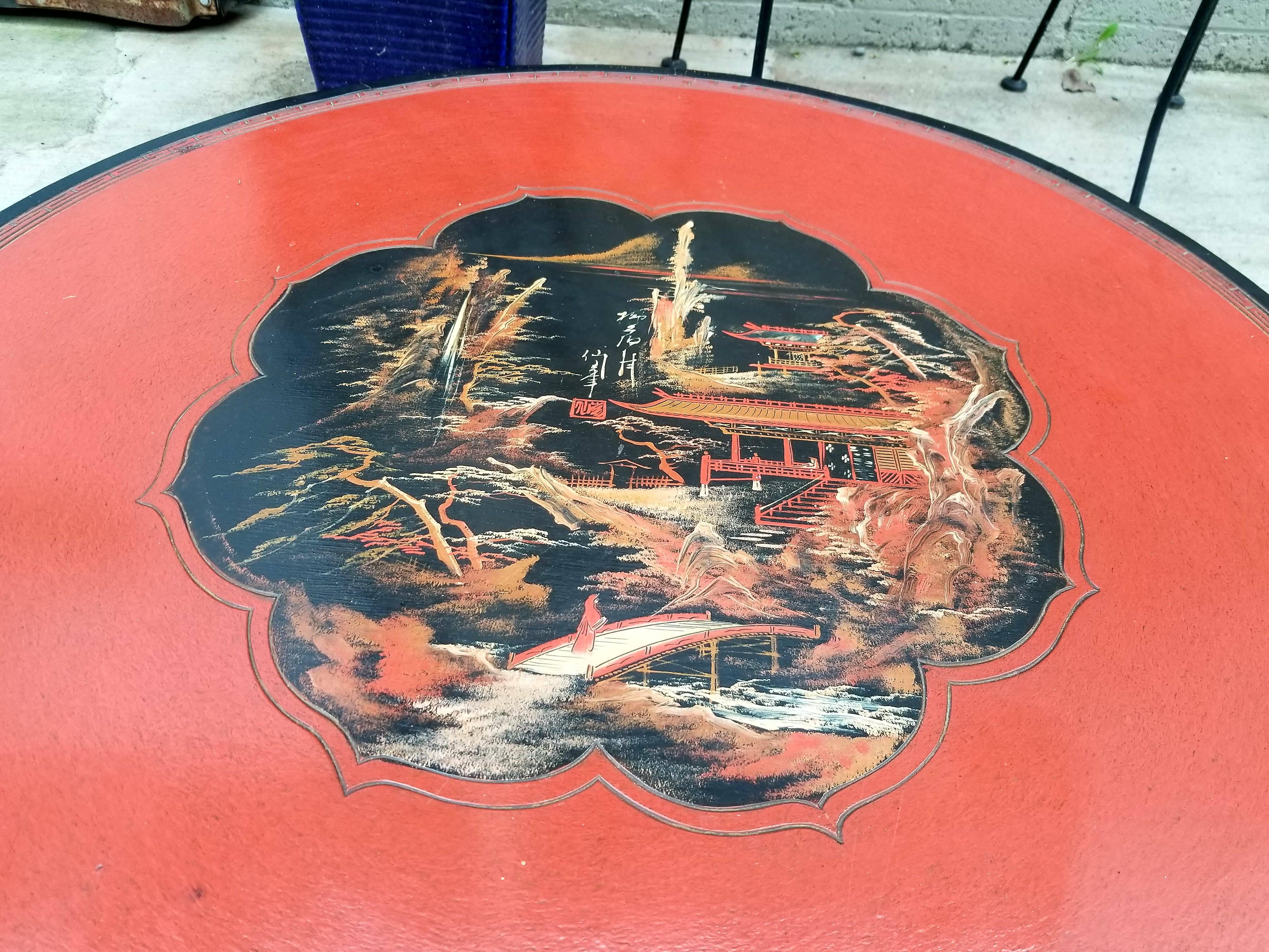 A red and black lacquer circular coffee table with a hand painted landscape and village scene. Mother-of-pearl inlay detail. Carved apron and legs, mid-20th century.
