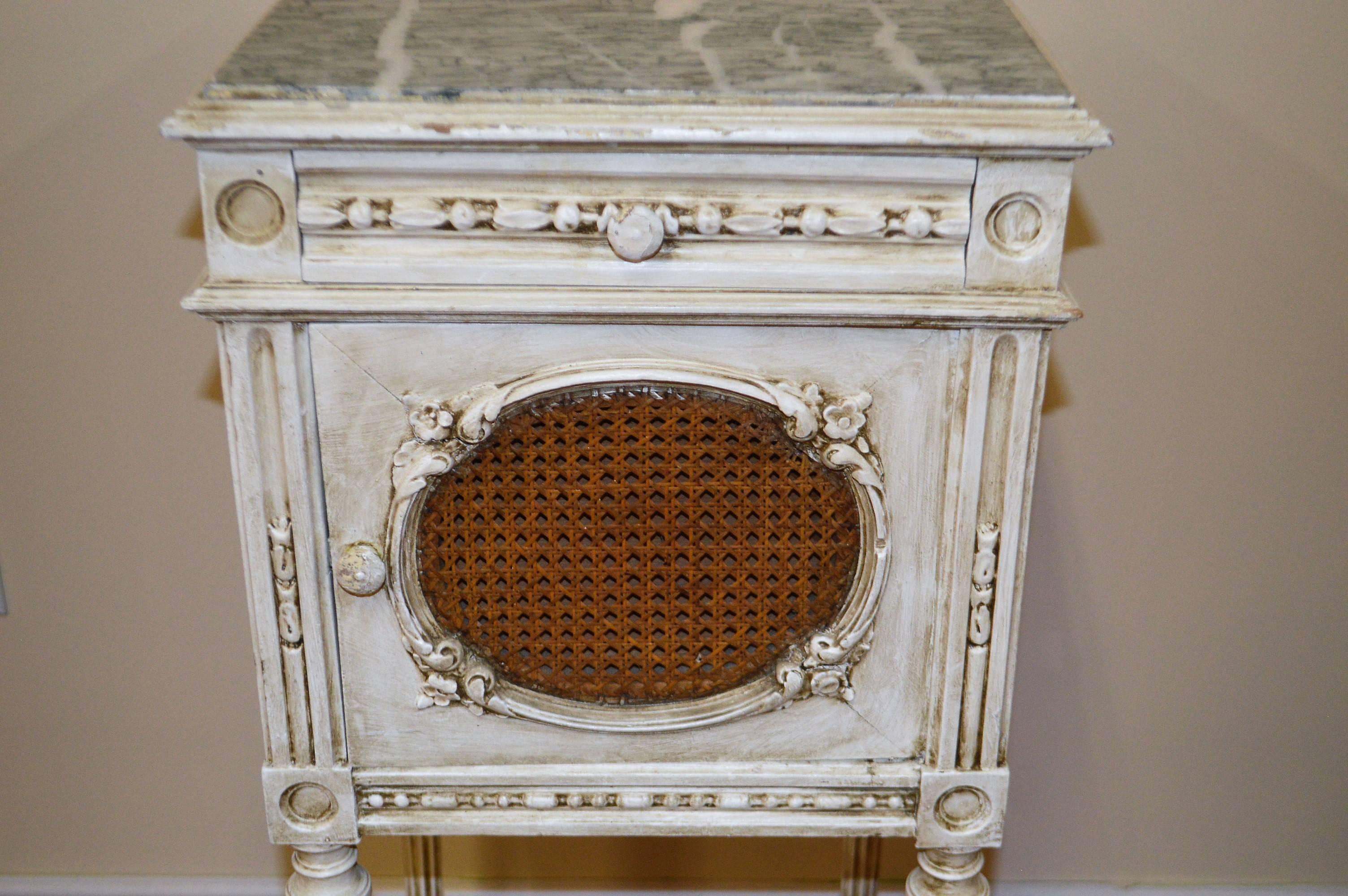 Very charming Louis XVI style painted nightstand or side table with a green and white marble top and caned medallion on front door.
It has a smaller drawer, a compartment for storage and a lower shelf.