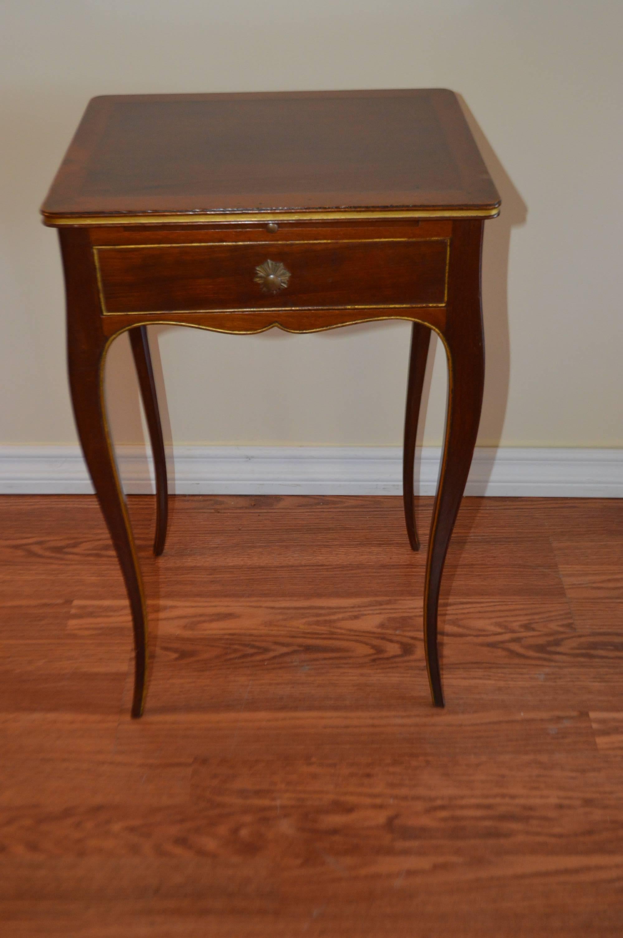 Most elegant and slender fine quality pair of mahogany side tables, having a fine gilded trace molding around all edges of the table. There is a small drawer and a pull-out leather top table above the drawer to hold a glass on each table.