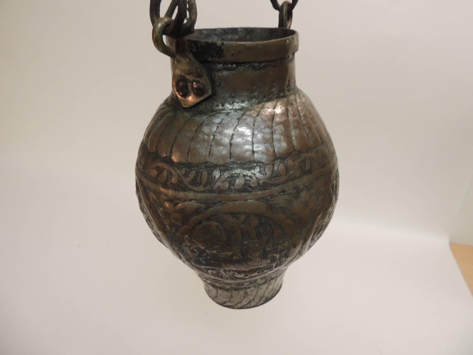 Offered by the Antique Textiles Galleries:
Antique Persian copper repousse oil lamp with hanging hook.  
Antique oil lamp designed with an intricate pattern and around three medallions that encircle the body of the vessel. The medallions depict a