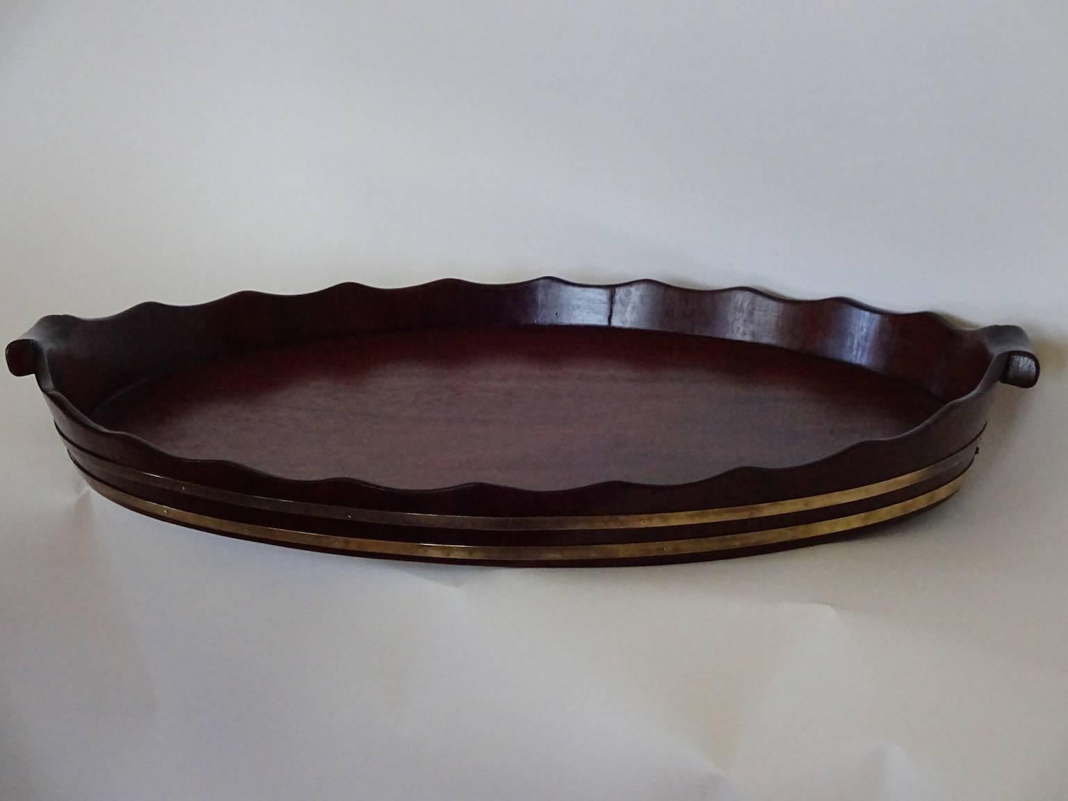 A wonderfully large double brass-banded George III mahogany tray with graceful fluted pie-crust edge and hand carved handles. Recently polished and ready to
serve. The height below includes the handles.