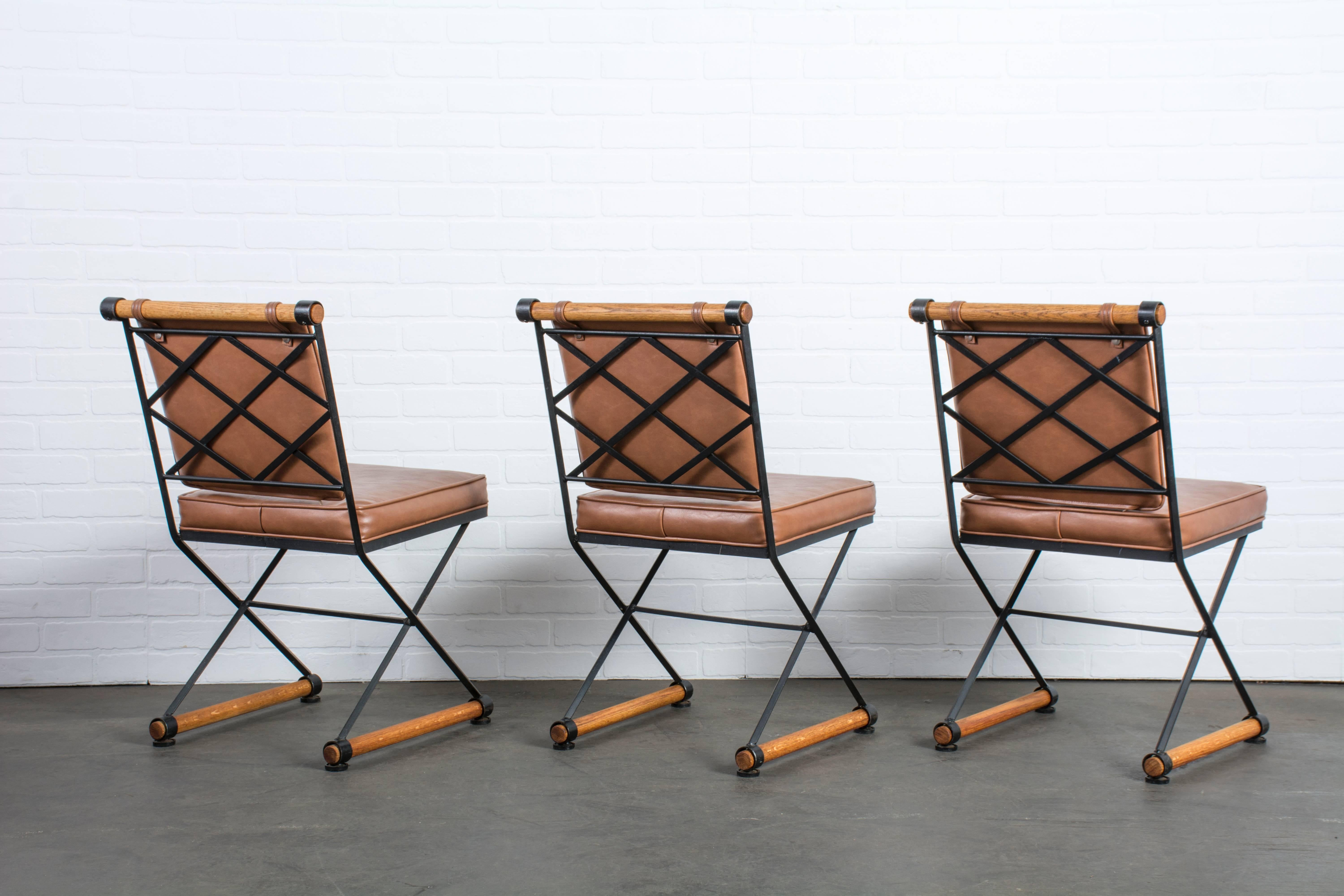 This is a set of six dining chairs that were designed by Cleo Baldon in the 1960s. They feature wrought iron frames, oak stretchers, and the original foam and brown Naugahyde upholstery. Original glides.