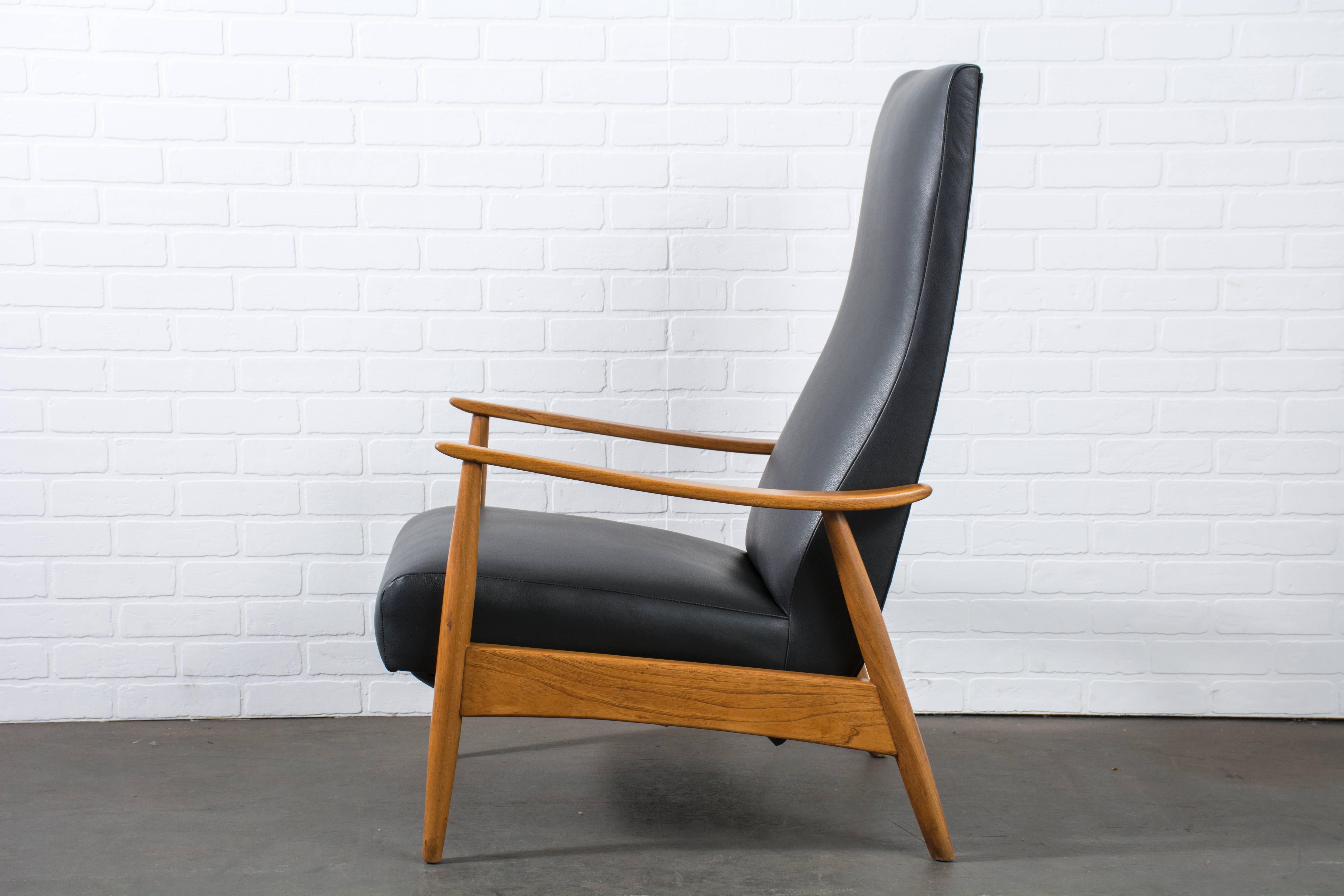 This Mid-Century Modern high back lounge lounge chair has an oak frame and has been professionally reupholstered in black leather. Reclining mechanism and built-in foot stool.