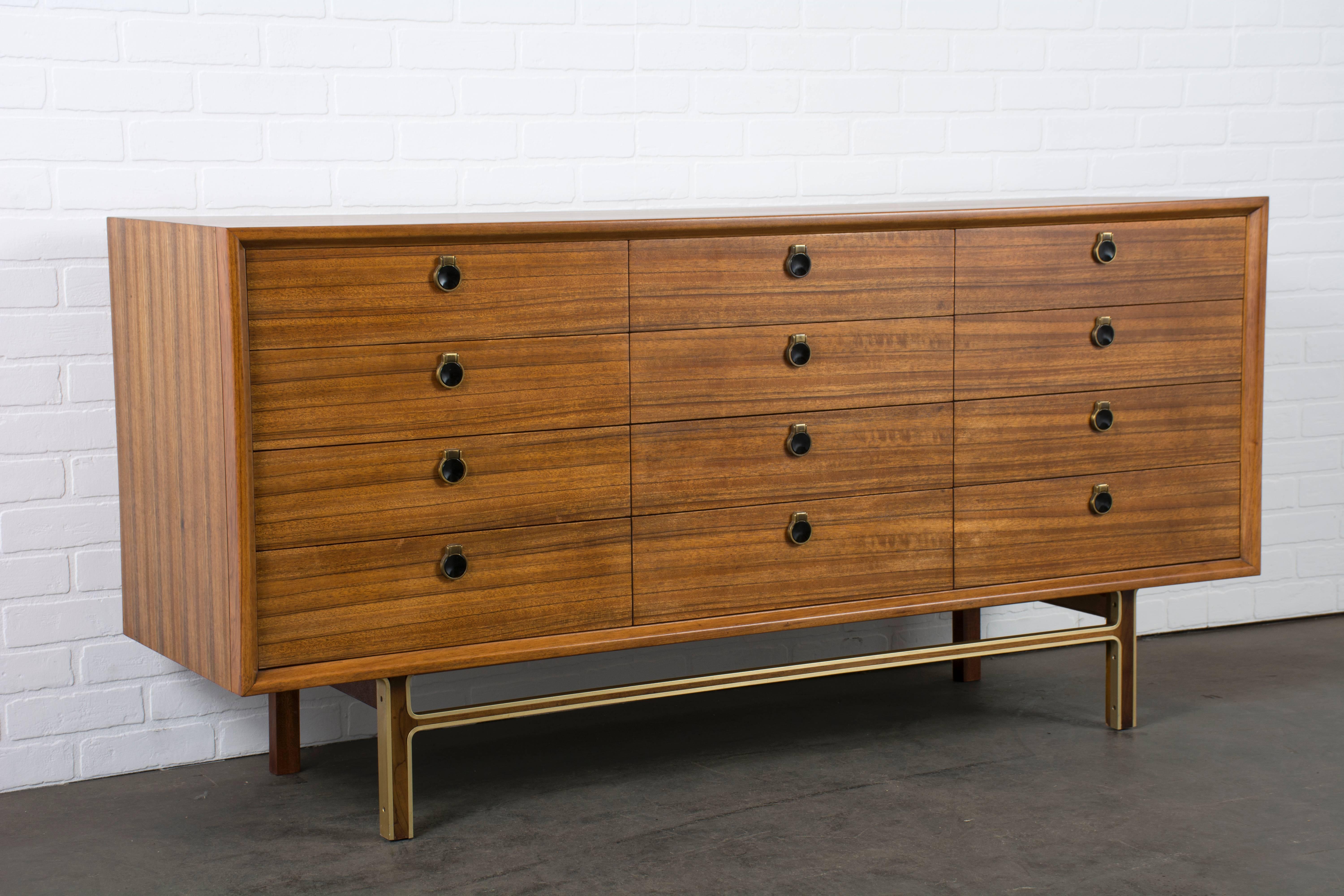 This Mid-Century Modern low mahogany dresser features 12 drawers (one drawer with dividers) and brass accents.