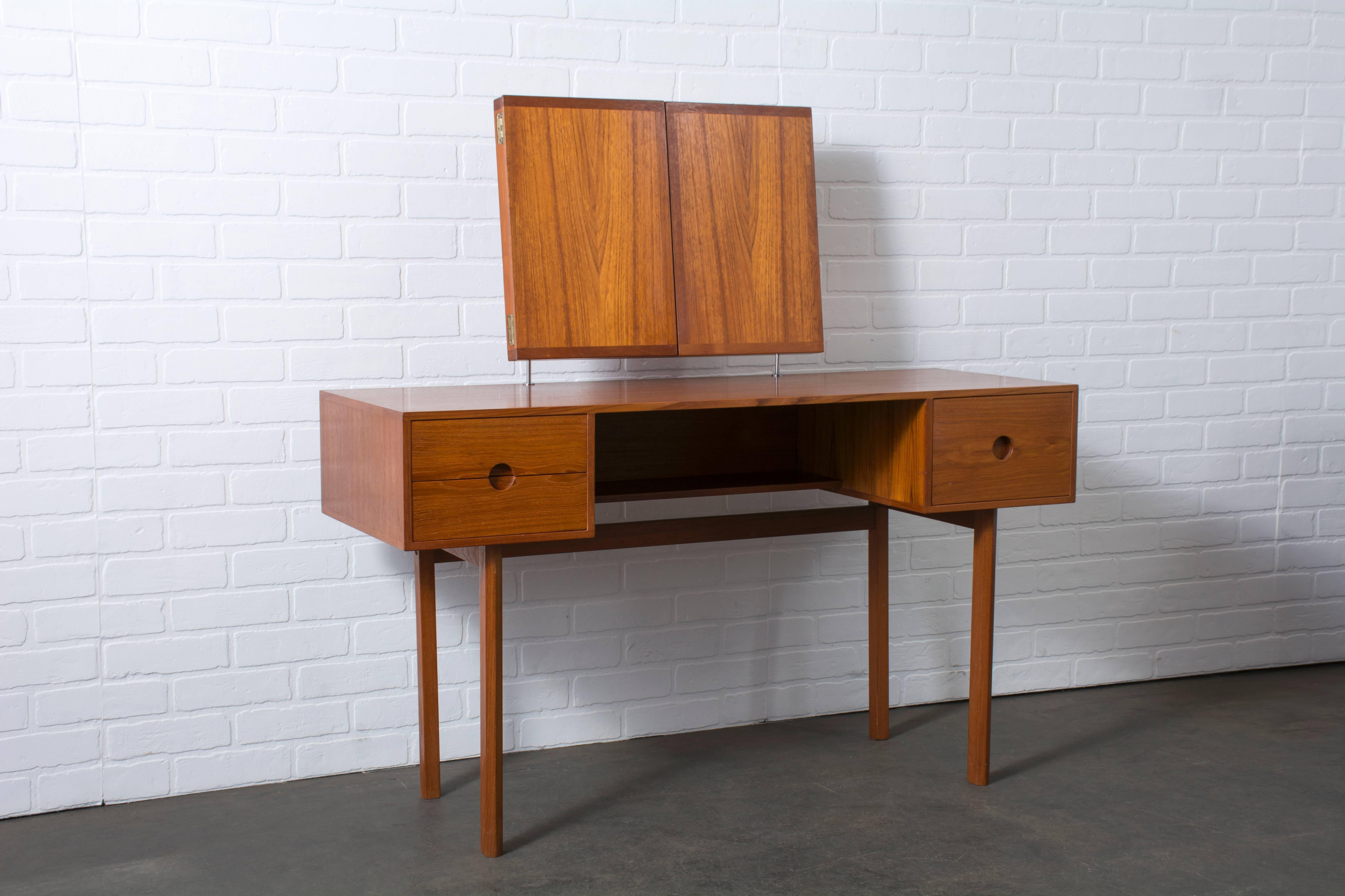 This vintage Mid-Century teak dressing table was designed by Kai Kristiansen for Aksel Kjersgaard/Illums Bolighus in the 1950s, Denmark. It features one deep drawer on the right, two smaller drawers on the left and one underlying shelf. The three