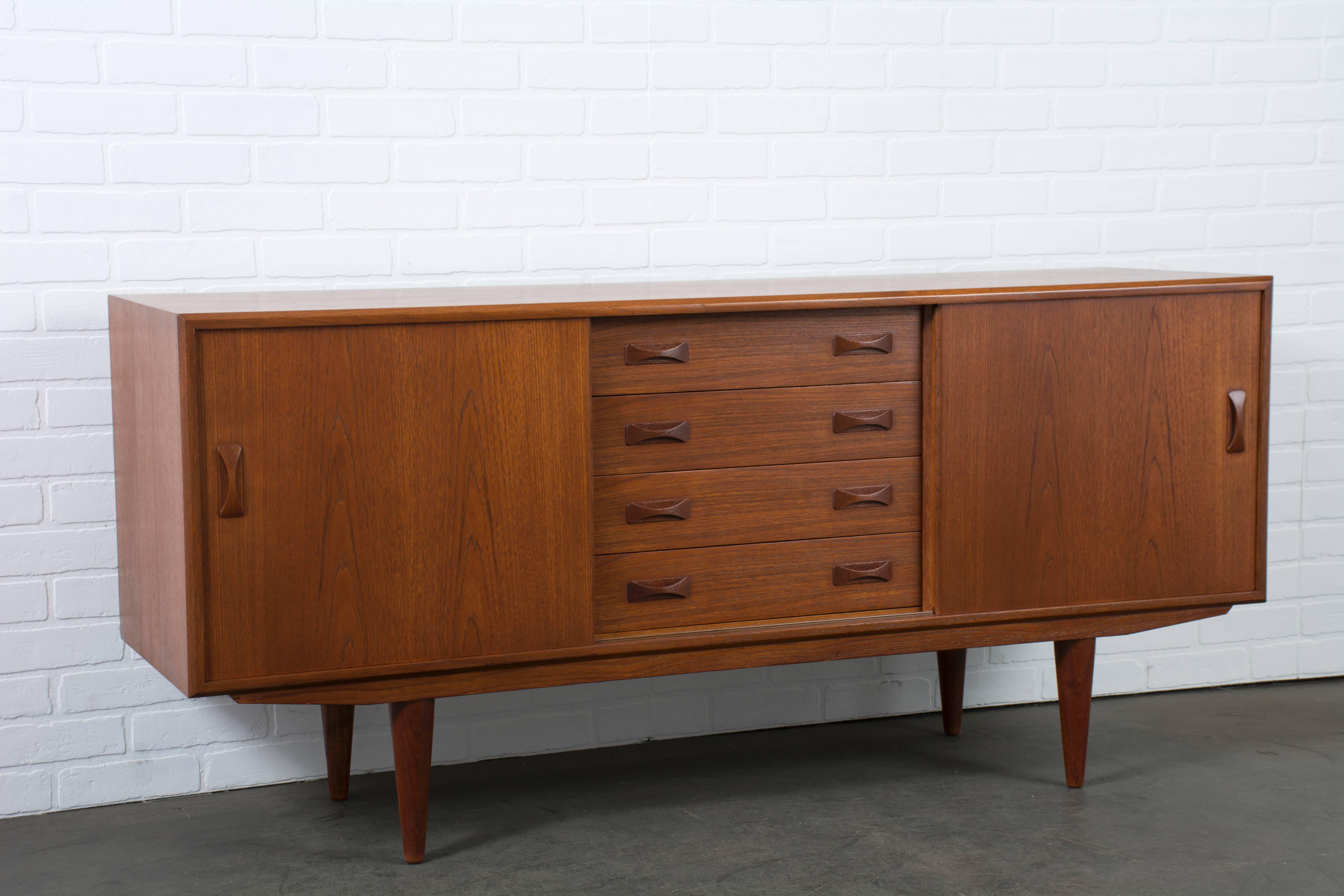 This Danish modern teak credenza was manufactured by Clausen & Son in the 1960s, Denmark. It features four drawers in the middle and sliding doors on each side that conceal one adjustable shelf.