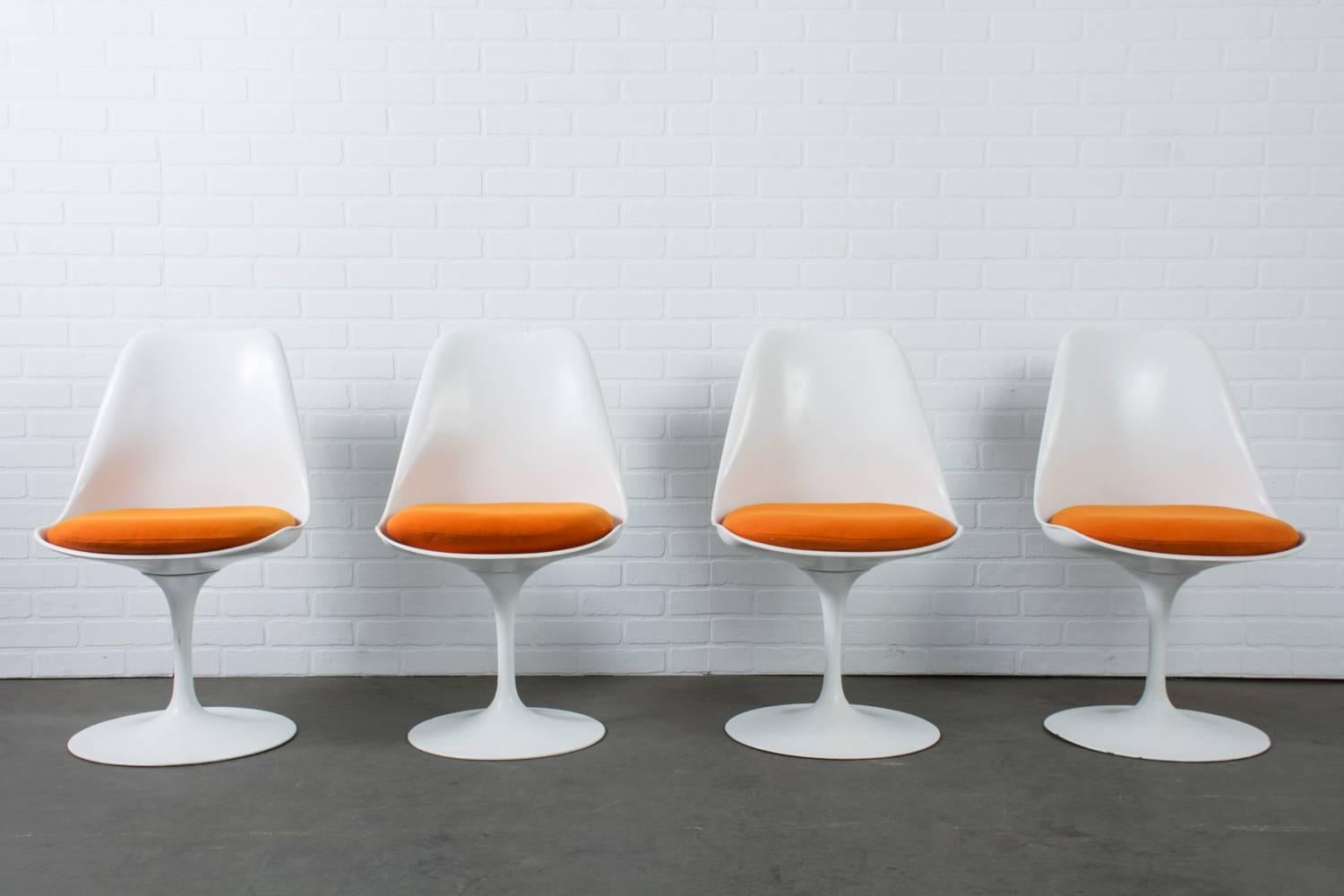 This is a set of four vintage Mid-Century Modern swivel tulip chairs designed by Eero Saarinen for Knoll in 1957.  They feature cast aluminum bases, molded fiberglass seat shells, and the original orange cushions.  Oval dining table and armchairs