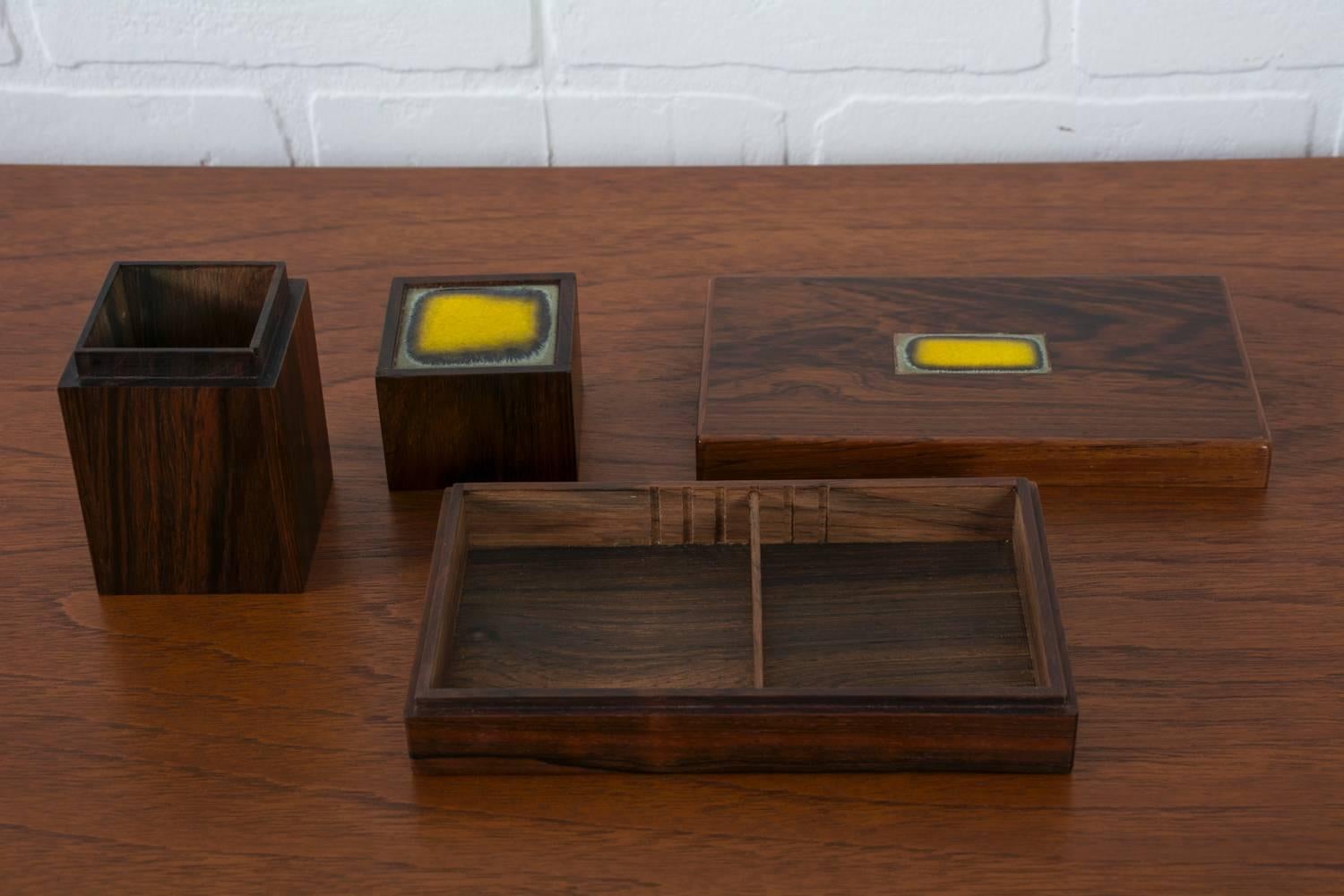 This set of two vintage Mid-Century solid rosewood boxes was designed by Bodil Eje for Alfred Klitgaard in the 1950s, Denmark. They each have a yellow ceramic tile inset in the lid. The flat box has an adjustable divider. Both boxes are stamped