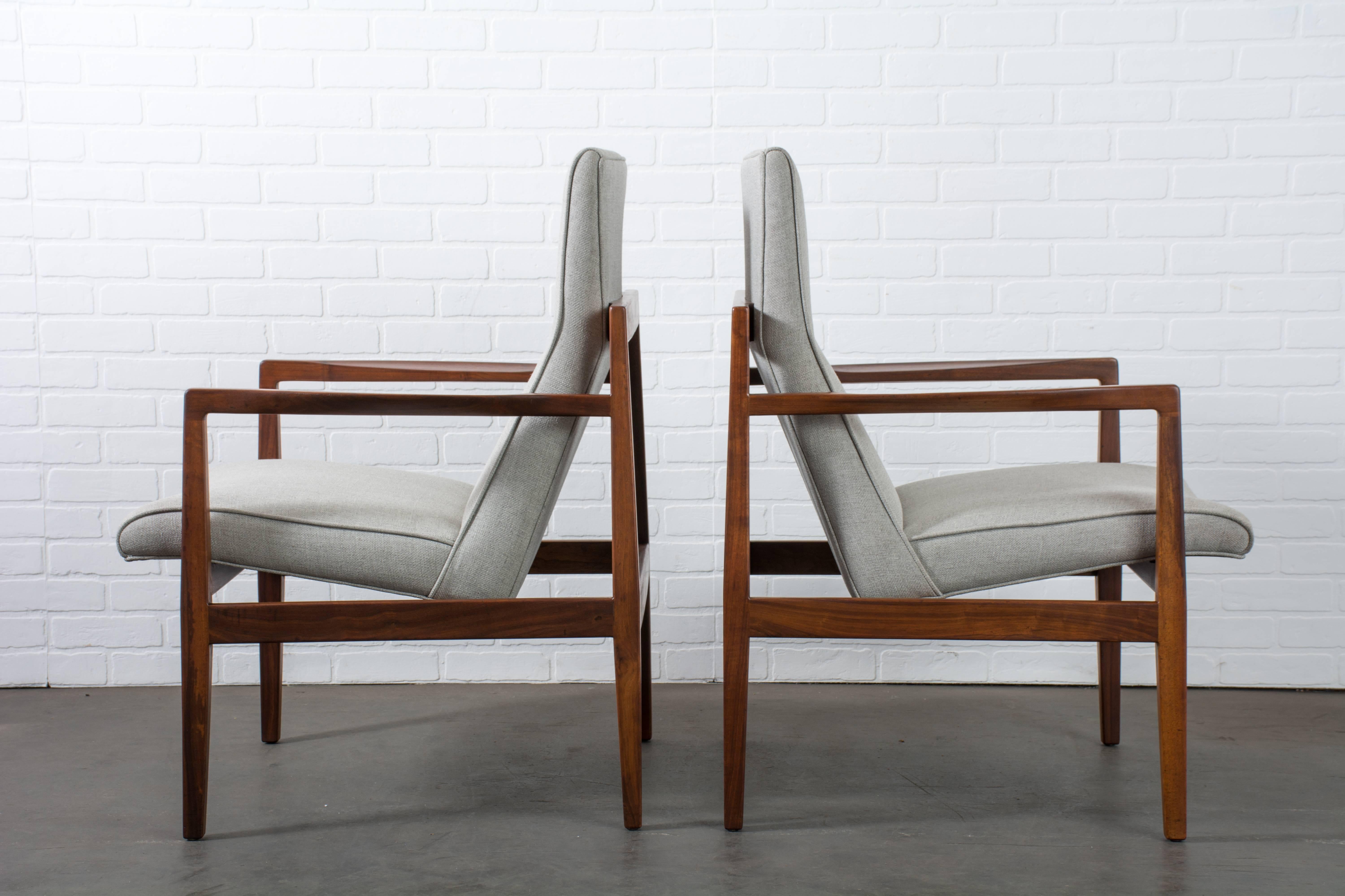 This pair of vintage Mid-Century lounge chairs was designed by Jens Risom for Jens Risom Design, Inc., USA, circa 1960. They feature sculptural walnut frames and floating seats upholstered in a light grey fabric.