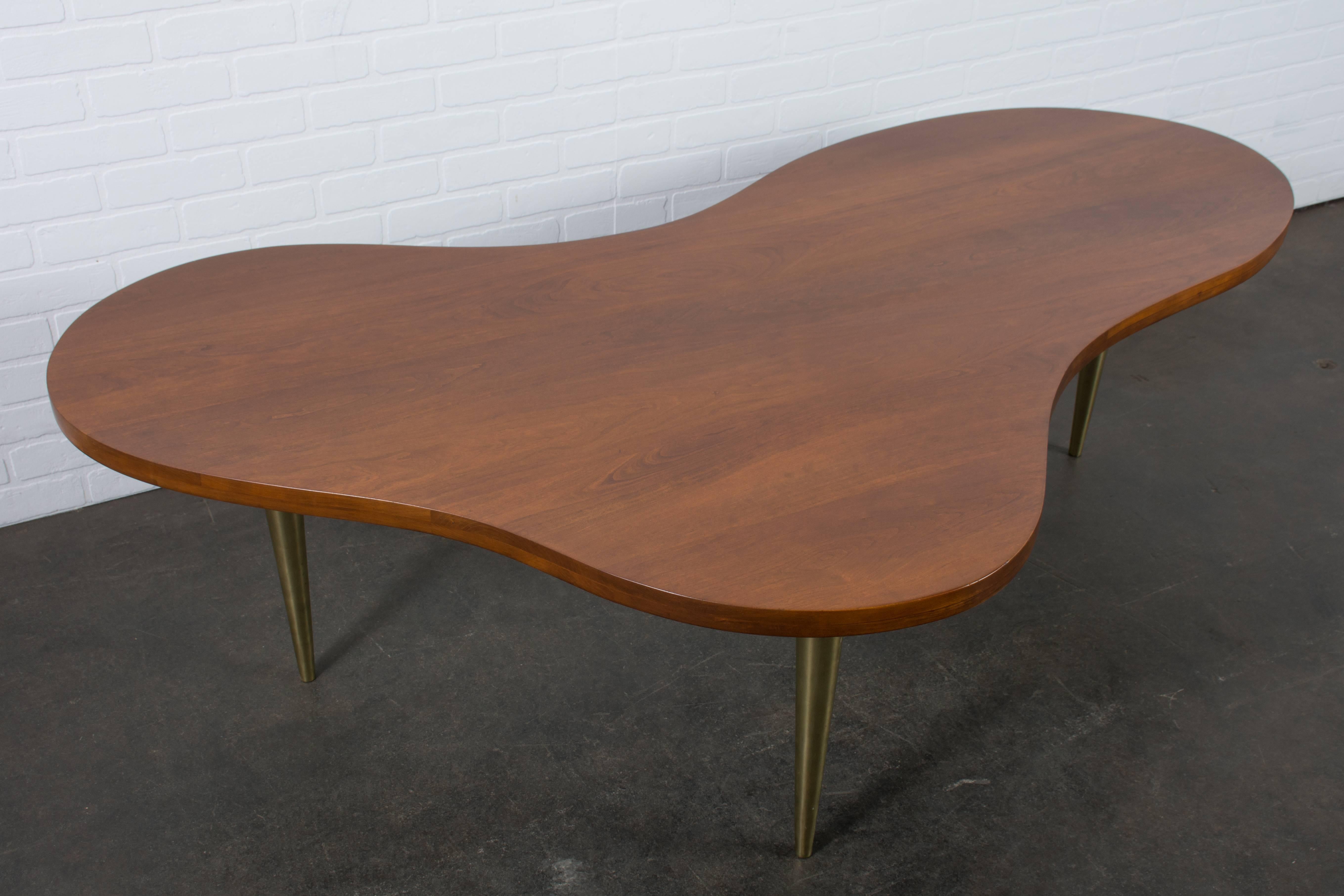 This vintage Mid-Century coffee table was designed by Terence Howard Robsjohn-Gibbings for Widdicomb in the 1950s. It features a metamorphic walnut top with the designer's signature softly contoured edges and three brass tapered legs. Widdicomb