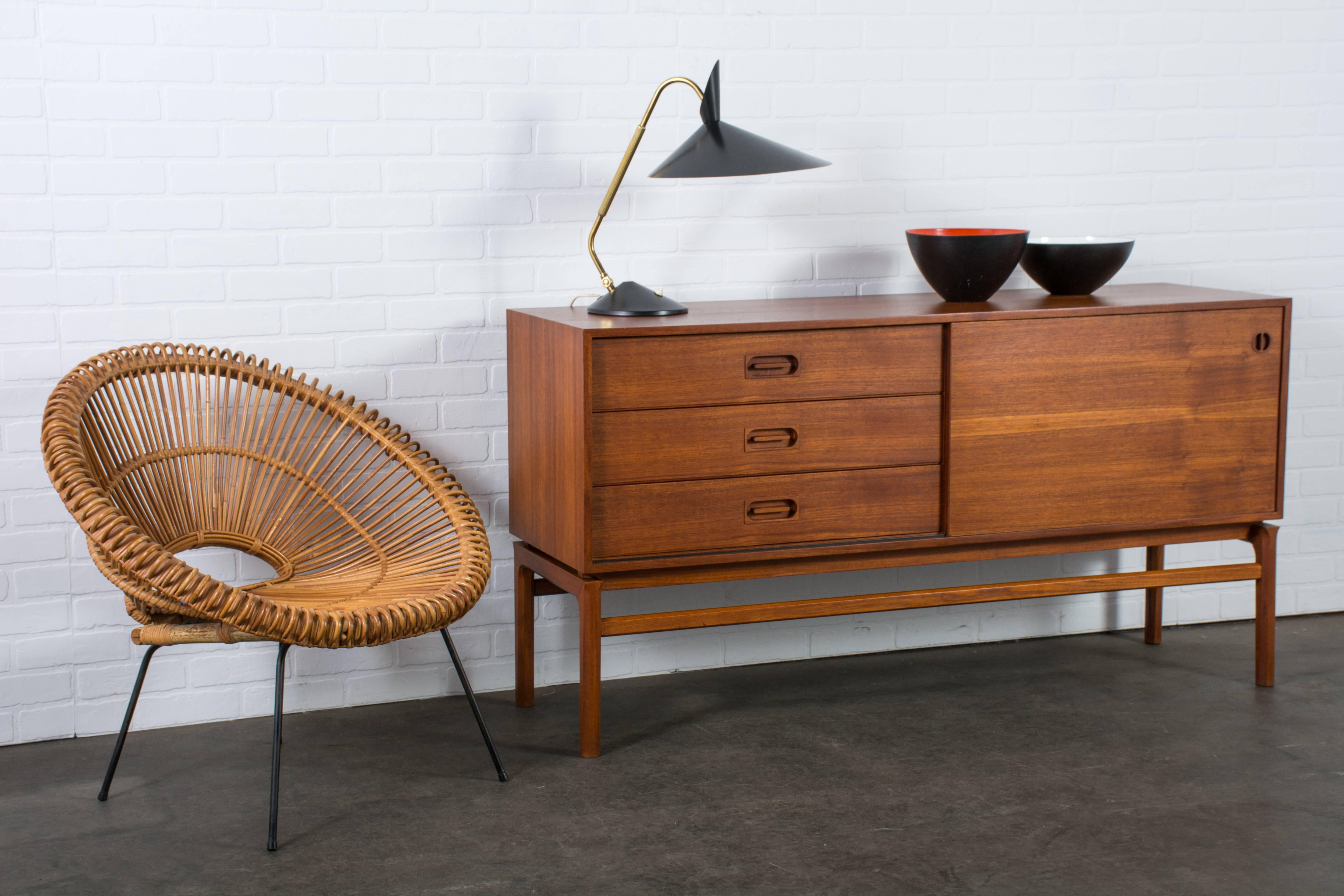 This vintage Mid-Century teak sideboard features three drawers on the left and a sliding door on the right that conceals one adjustable shelf. Marked Borchorst & Lindhard, Made in Denmark, 1958.