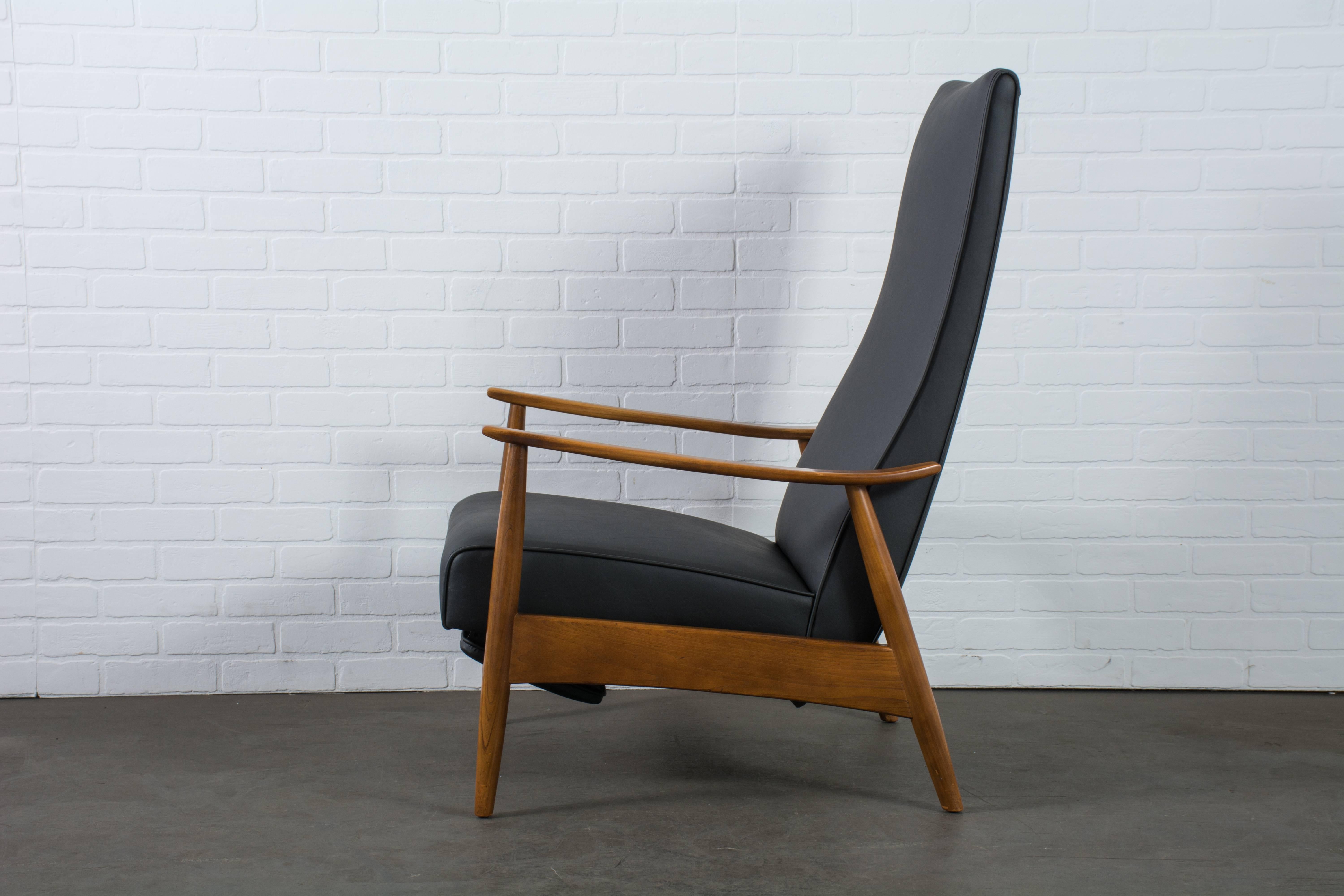 This Mid-Century Modern high back reclining lounge chair was designed by Milo Baughman in the 1960's. It has an oak frame and has been professionally reupholstered in black naugahyde. When used in a reclined position, the upholstered footrest comes
