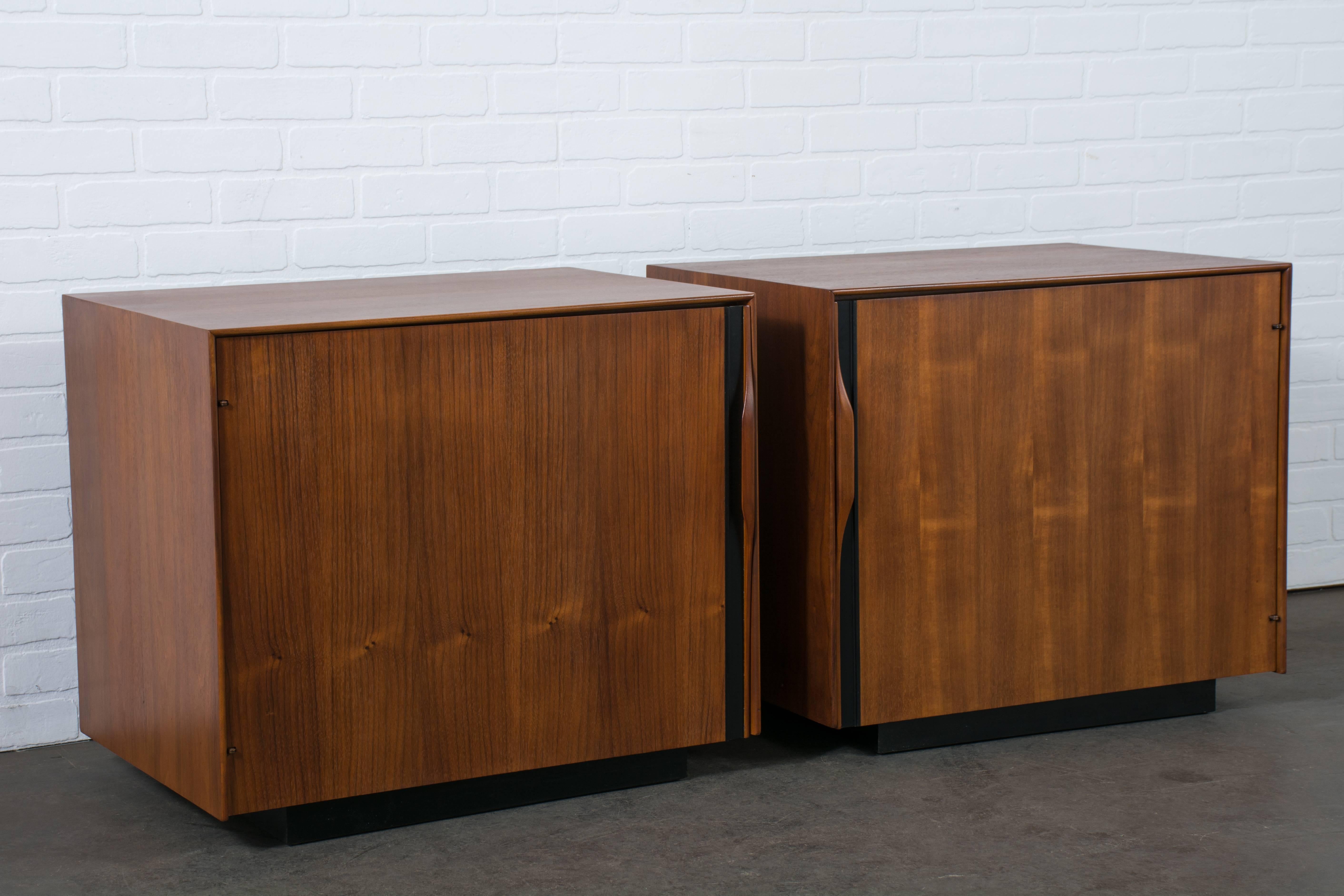 These Mid-Century Modern walnut nightstands were designed by John Kapel for Glenn of California in the 1960s. Each cabinet features plenty of storage with a shelf, magazine holder, and pull-out white laminate tray. The black details contrast