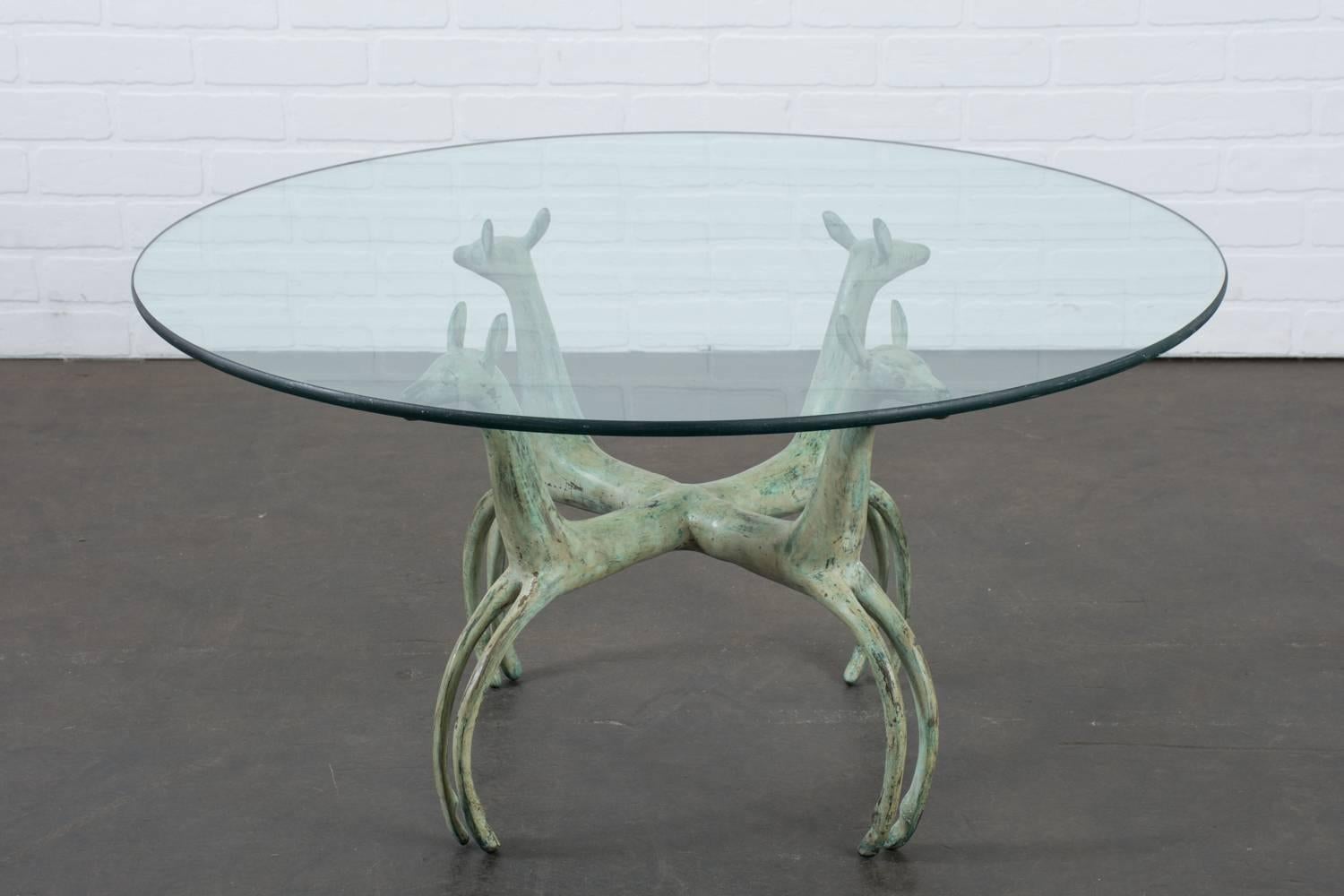 This vintage coffee table is the manner of Armand Albert Rateau. It features a bronze base that is made up of four joined deer with a wonderful green patina and a round glass top.
