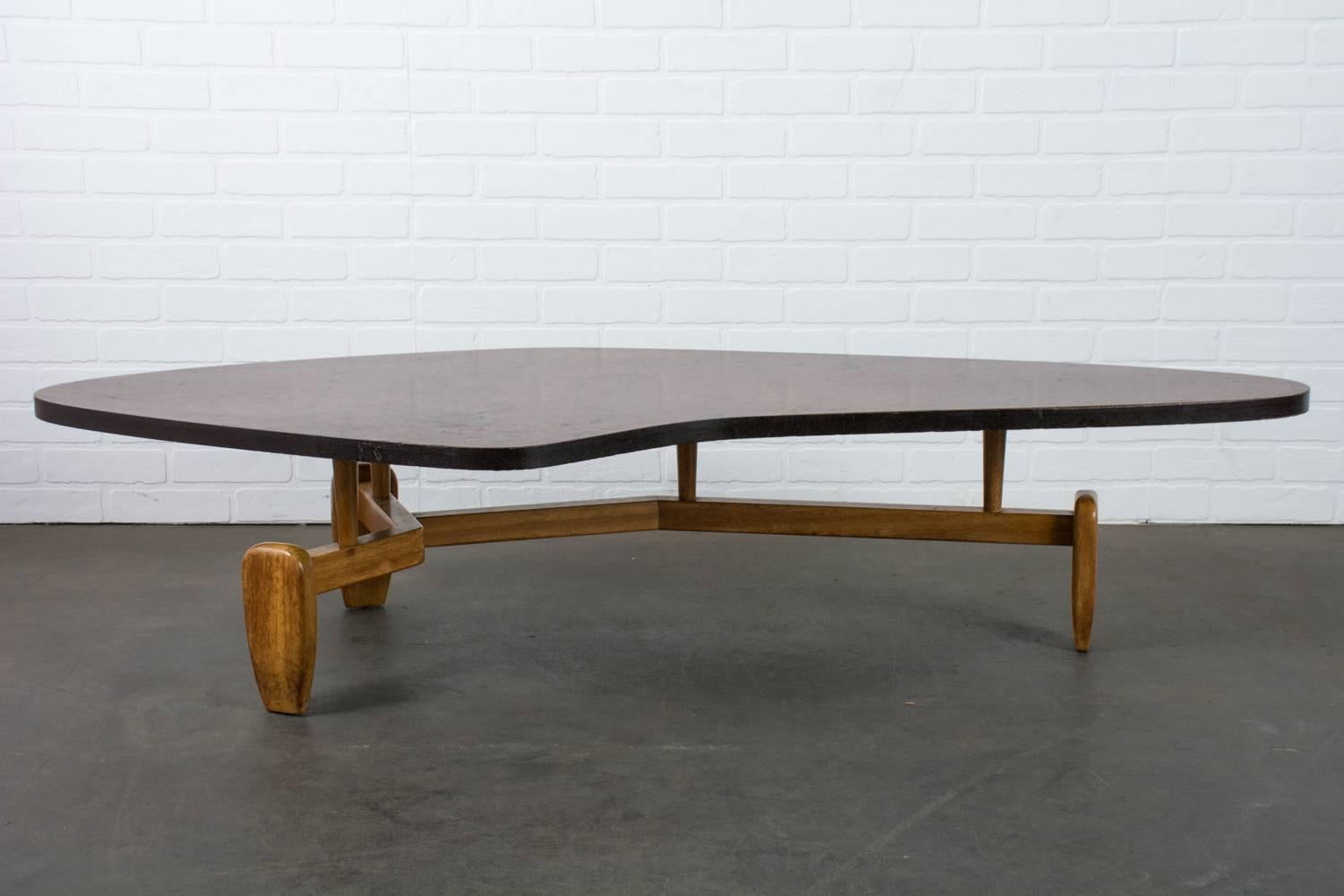 This Mid-Century Modern coffee table was designed by John Keal for Brown Saltman in the 1950s. The boomerang/amoeba style floating top is a made of a composite wood that has an interesting variation in tones. The sculptural legs and stretchers are