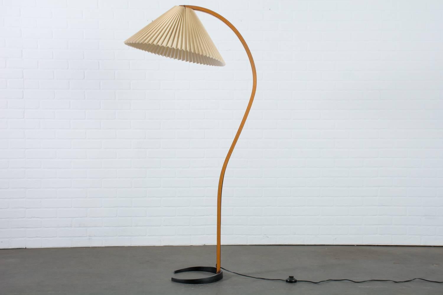 This vintage Mid-Century floor lamp was designed by Mads Caprani for Caprani Light AS. It features a sculptural bent plywood Stand with an elegant curve, a cast iron crescent shaped base, and the original pleated linen shade. Stamped 'Caprani Light'