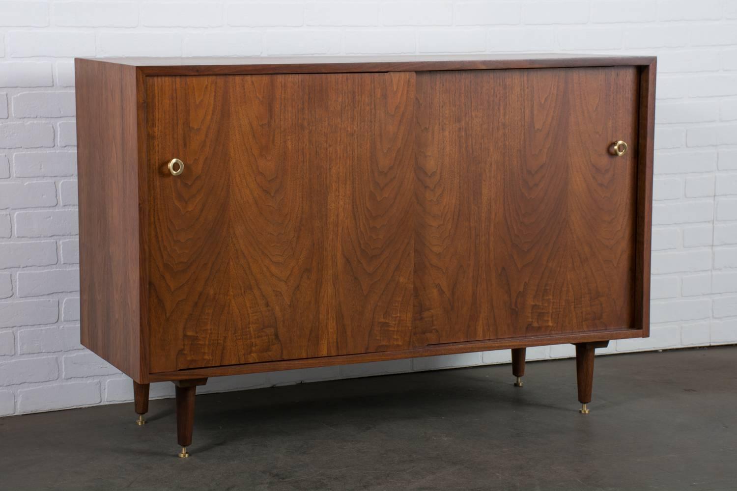 This vintage Mid-Century walnut credenza was designed by Greta Grossman for Glenn of California in the 1950's. It features two sliding doors that conceal one adjustable shelf on the left and four orange lacquered drawers on the right. Beautiful