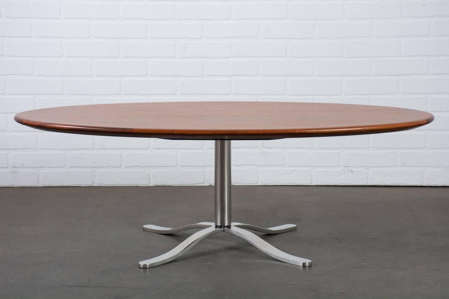 This Mid-Century Modern coffee table by Dunbar features an oval teak top with a bevelled edge and a polished stainless steel 'X' base. Dunbar label underneath.
