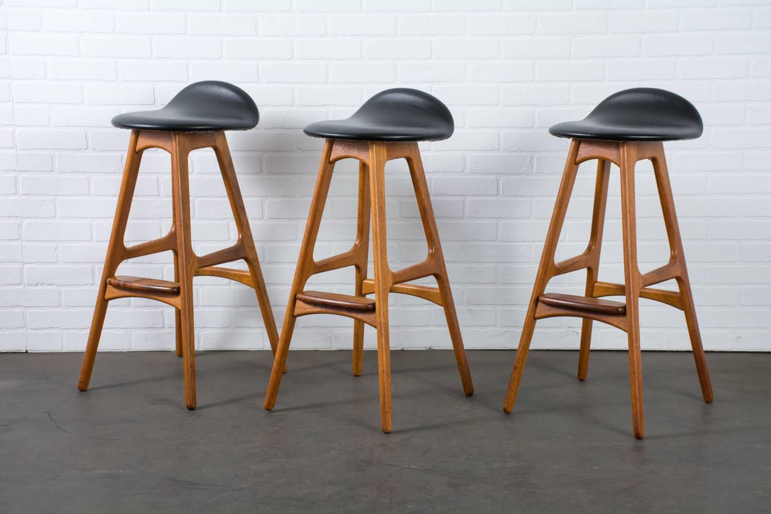 These vintage Mid-Century bar stools were designed by Erik Buch (also known as Erik 'Buck' in English), circa 1960s, Denmark. The frames are teak with a rosewood foot rest. These stools have the original black Naugahyde upholstery.