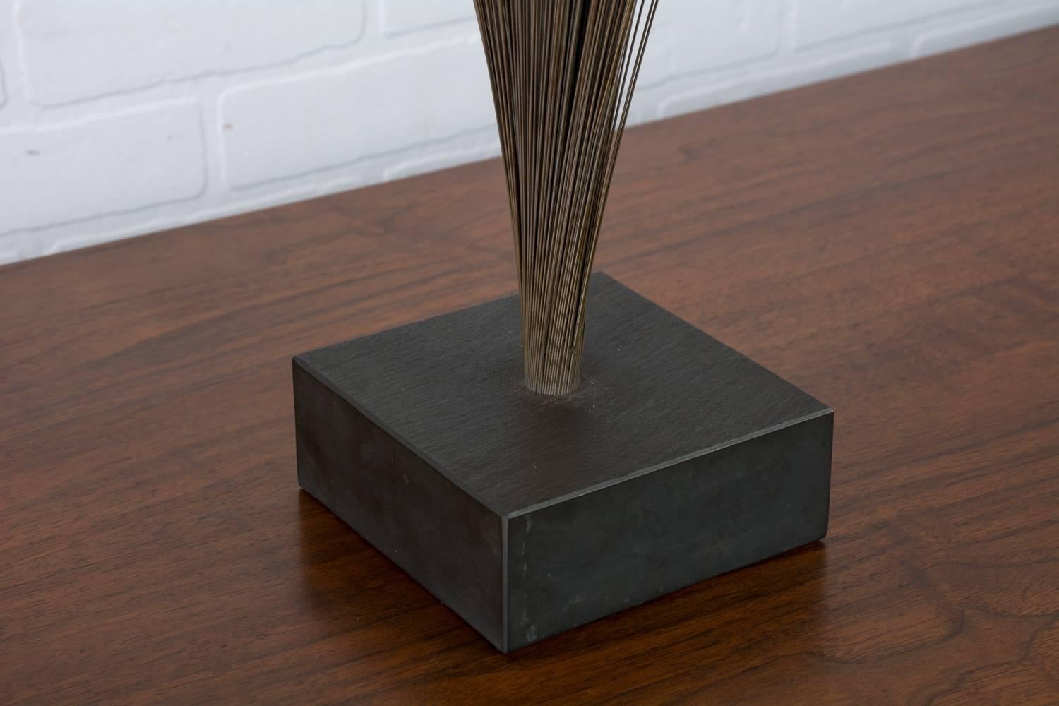 This vintage midcentury sculpture is in the style of Harry Bertoia's spray sculpture. It features a slate base and metal rods with a bronze finish that 'spray' out from the base.